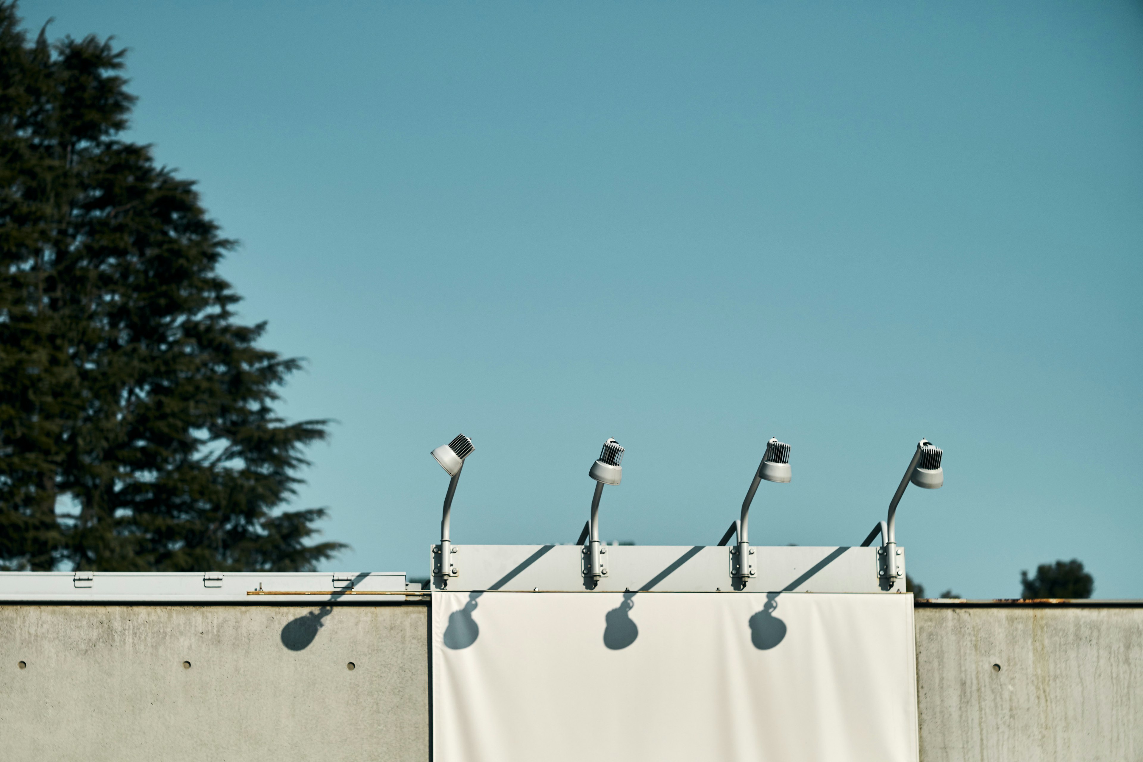 Muro de concreto con una tela blanca y múltiples luces bajo un cielo azul