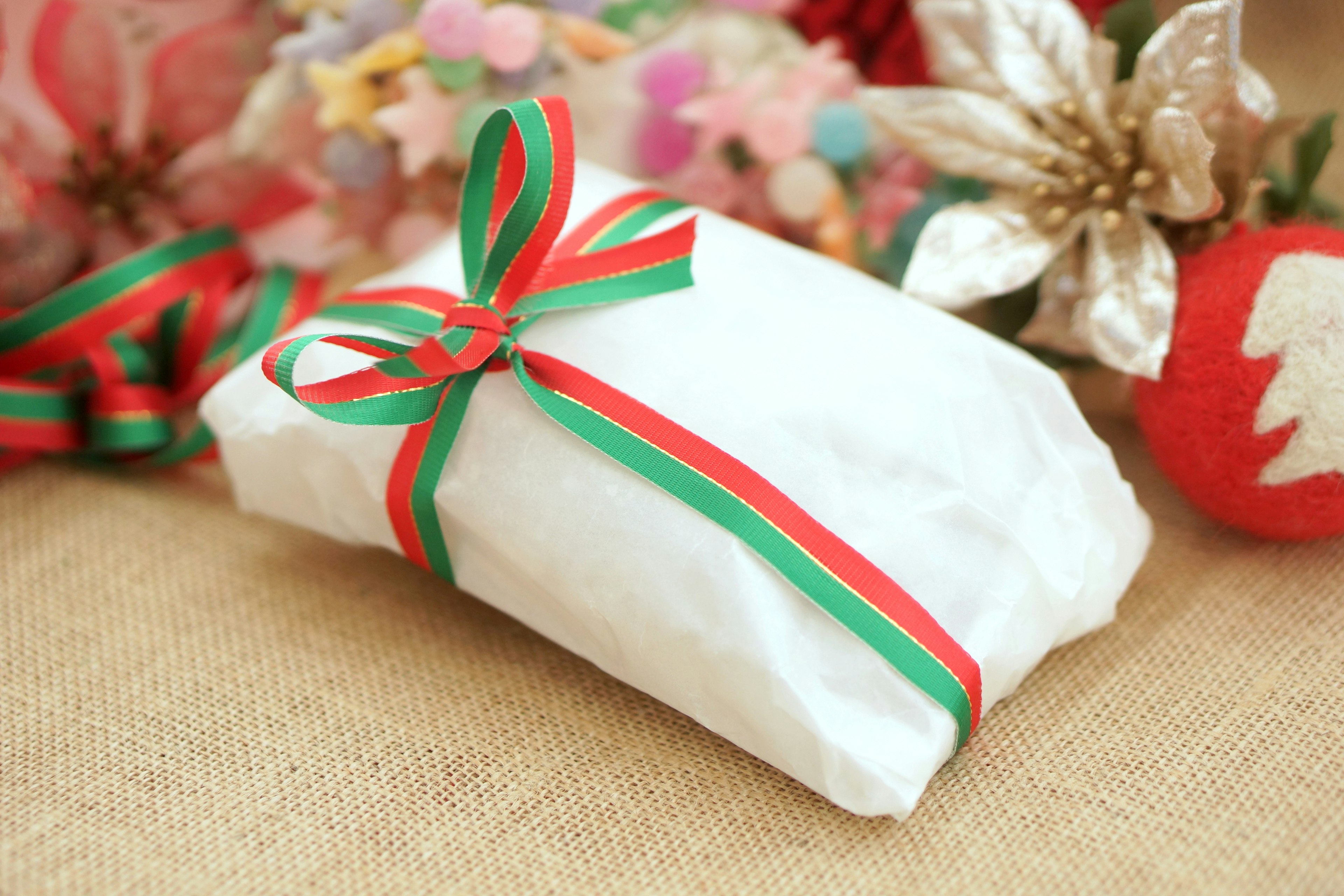 A gift wrapped in white paper with a green and red ribbon