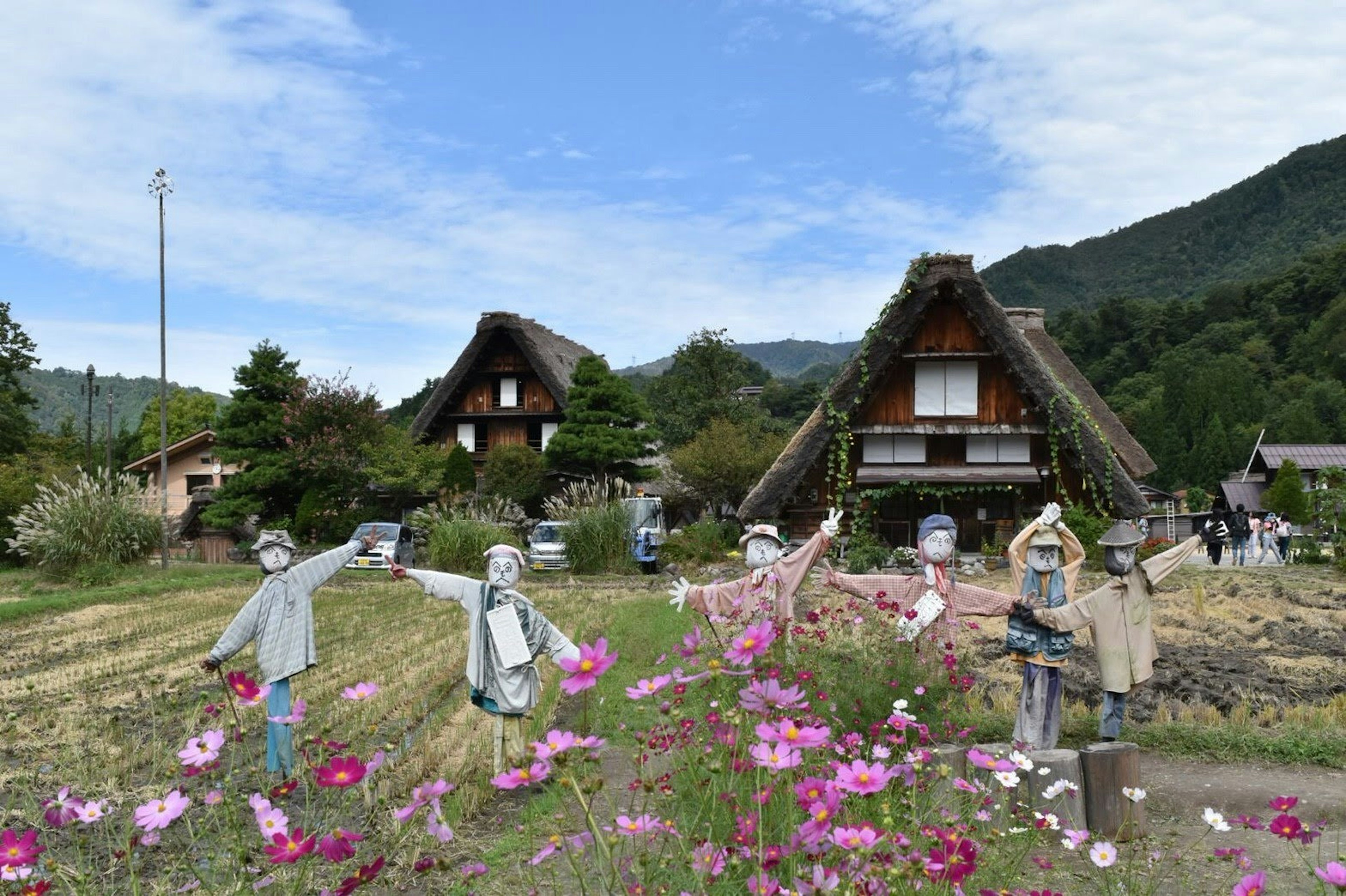 傳統合掌式房屋坐落在鄉村風景中，前景有五彩繽紛的花朵