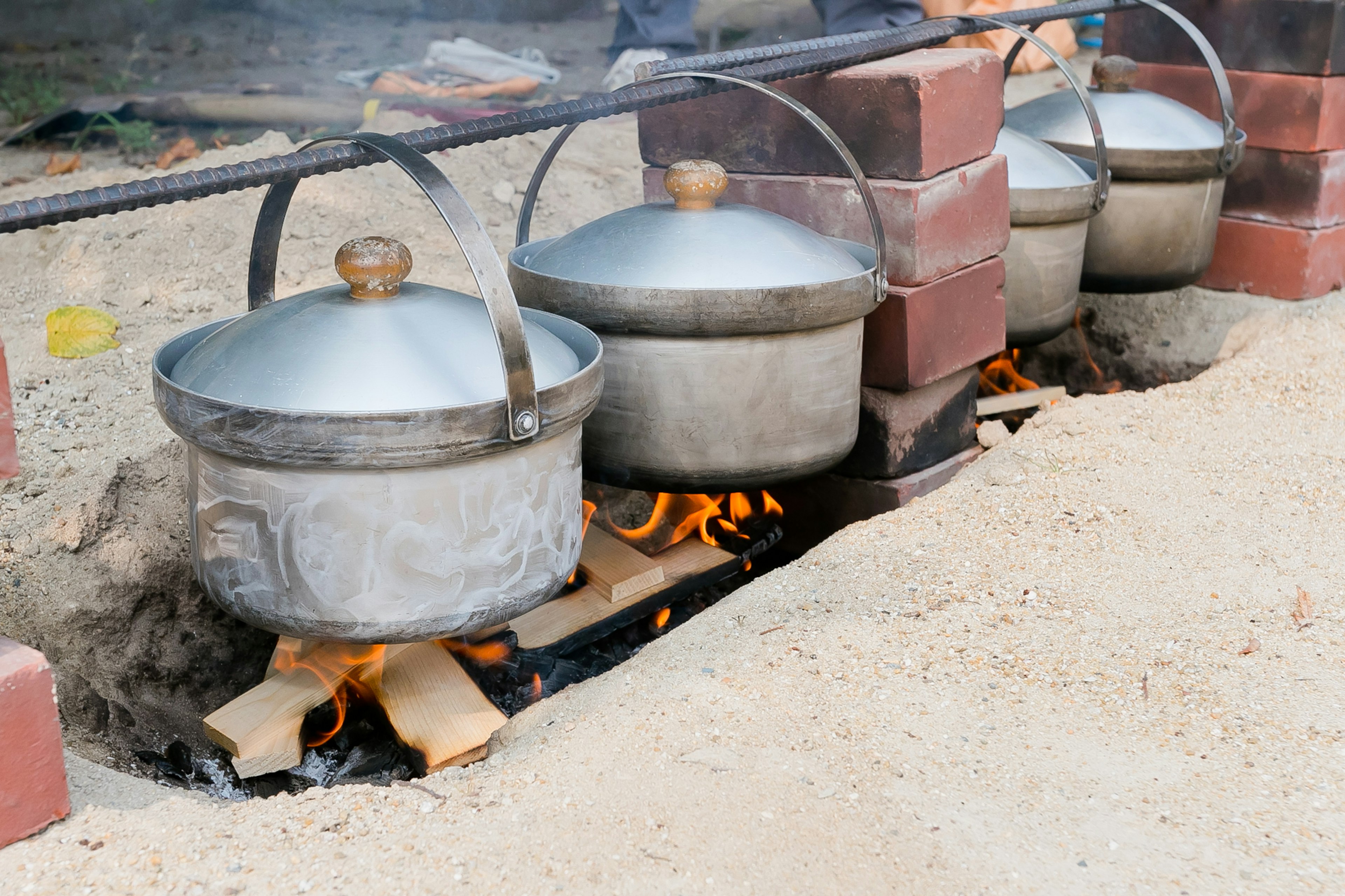 Reihe von Metalltöpfen, die über einem Feuer im Freien kochen Rauch steigt von den Töpfen auf