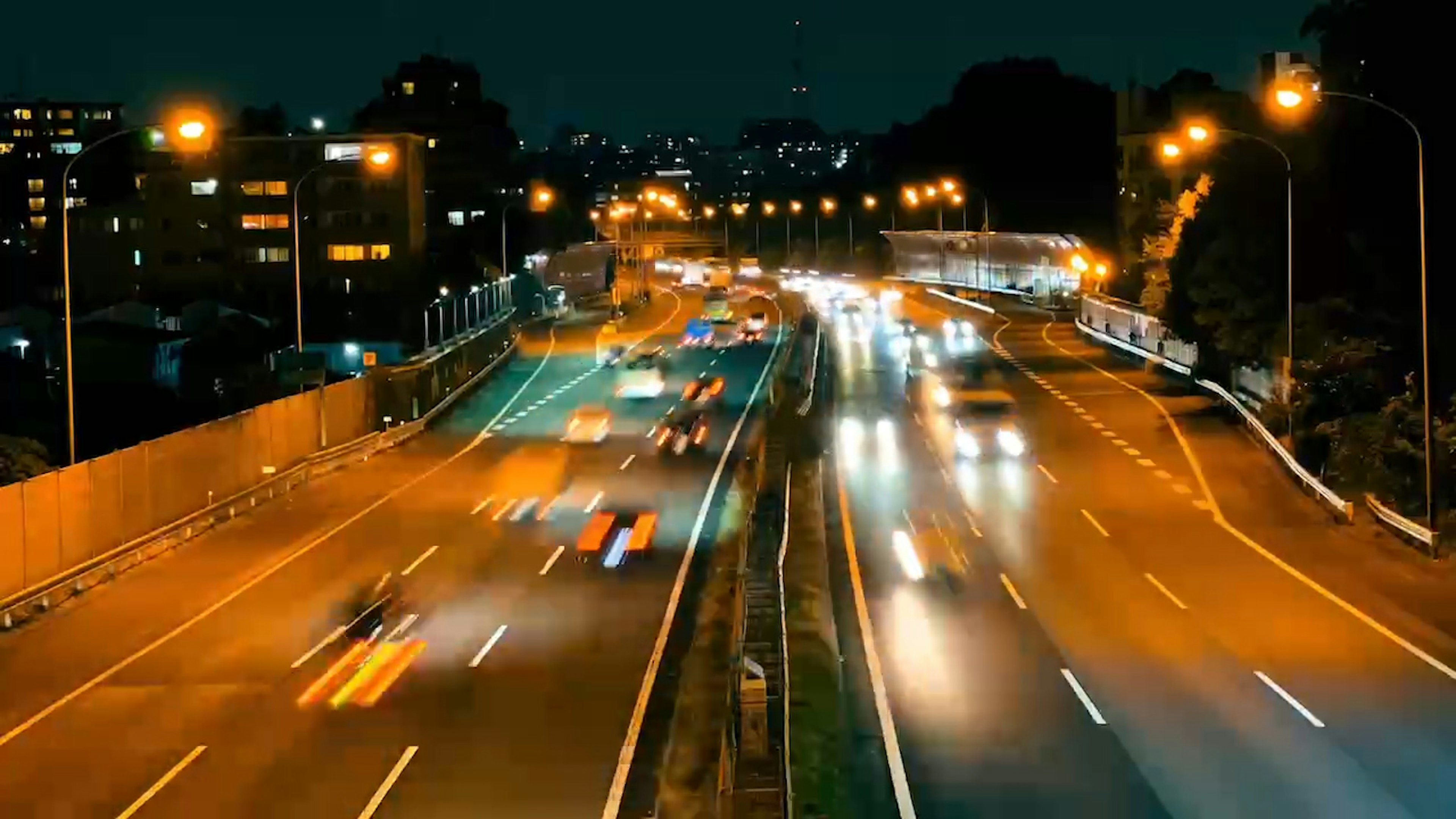 Autopista nocturna con luces de coches en movimiento y horizonte de la ciudad