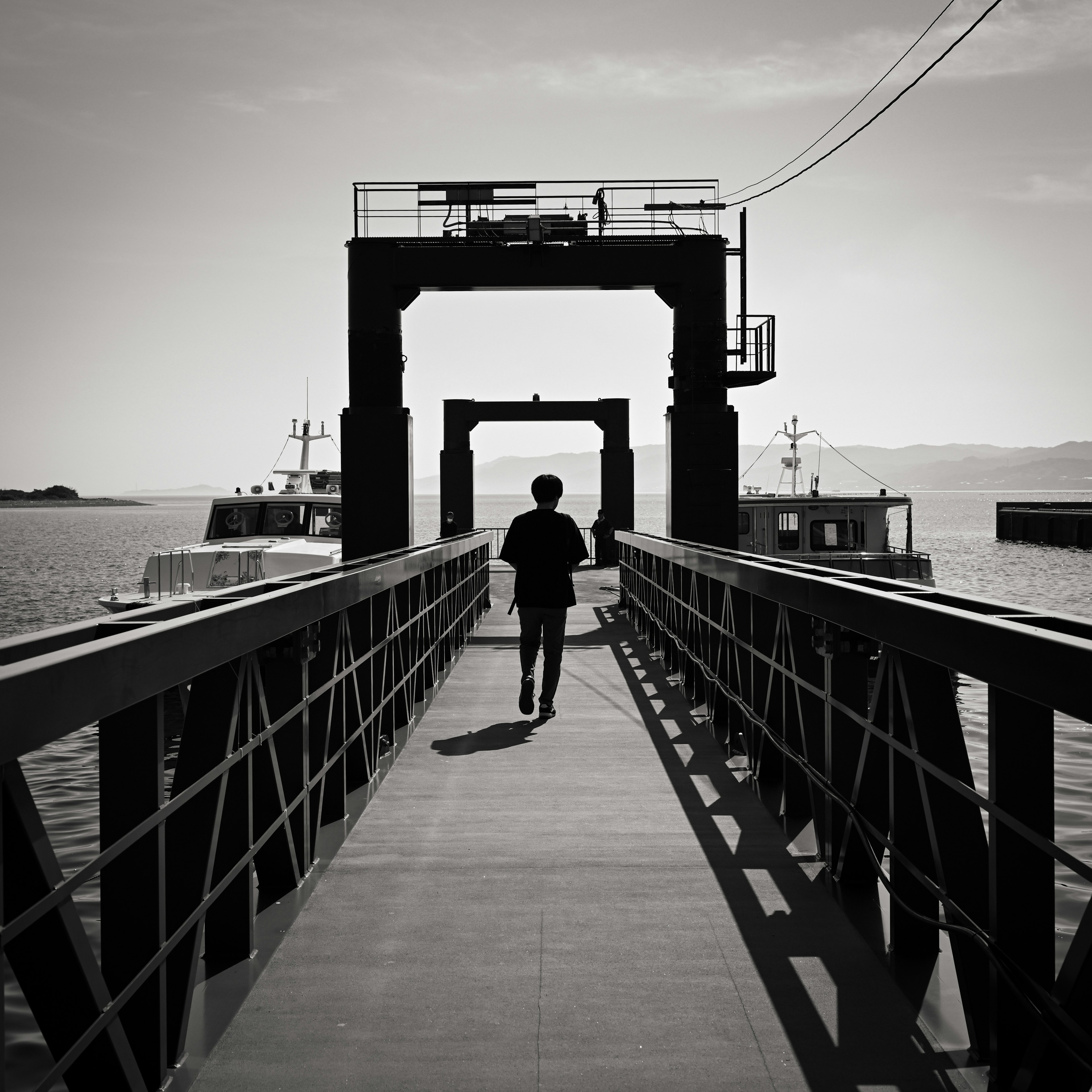 Persona caminando en un muelle en blanco y negro con barcos al fondo