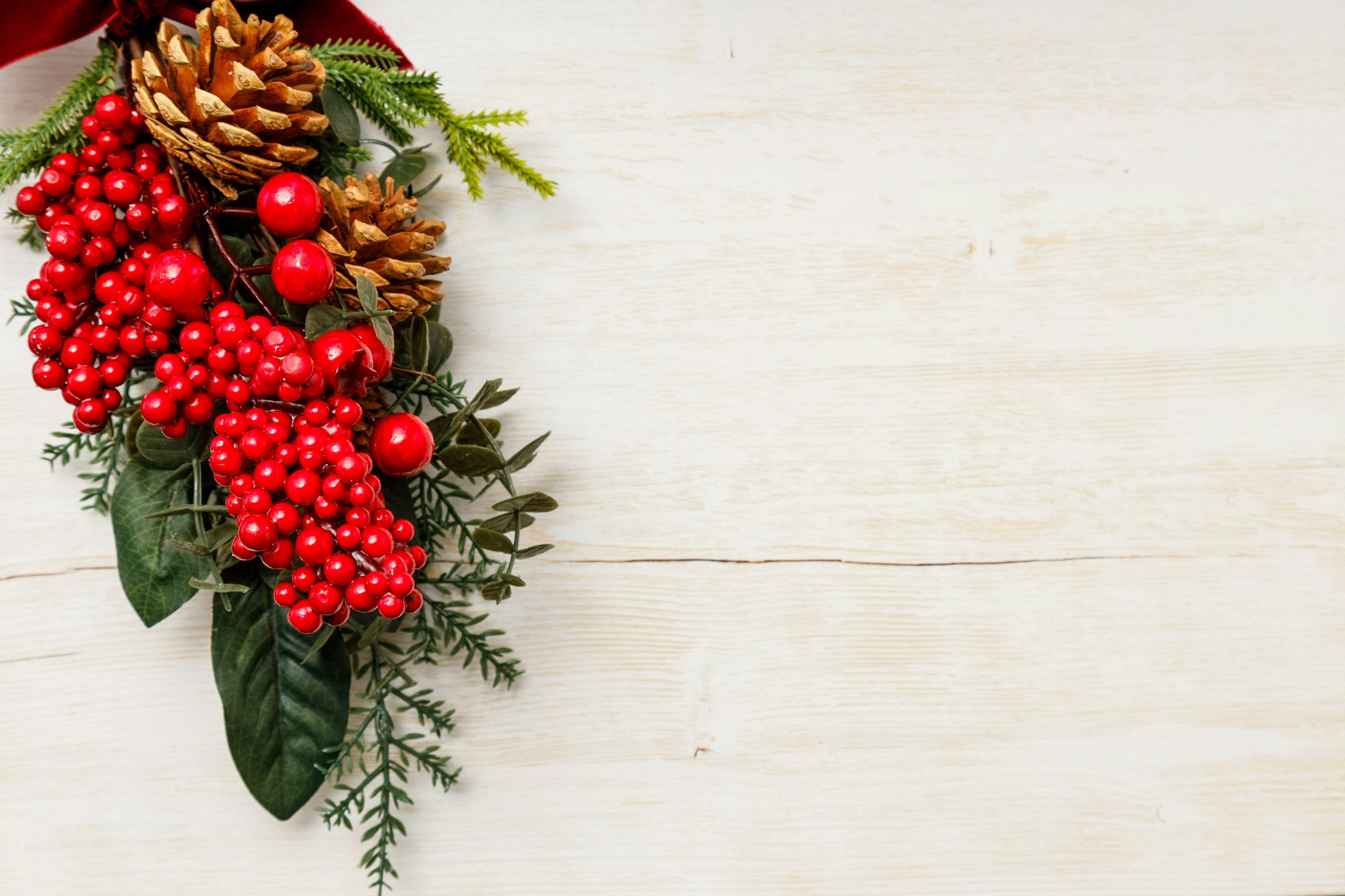 Weihnachtsdekoration mit roten Beeren und Tannenzapfen auf einem weißen Holztisch