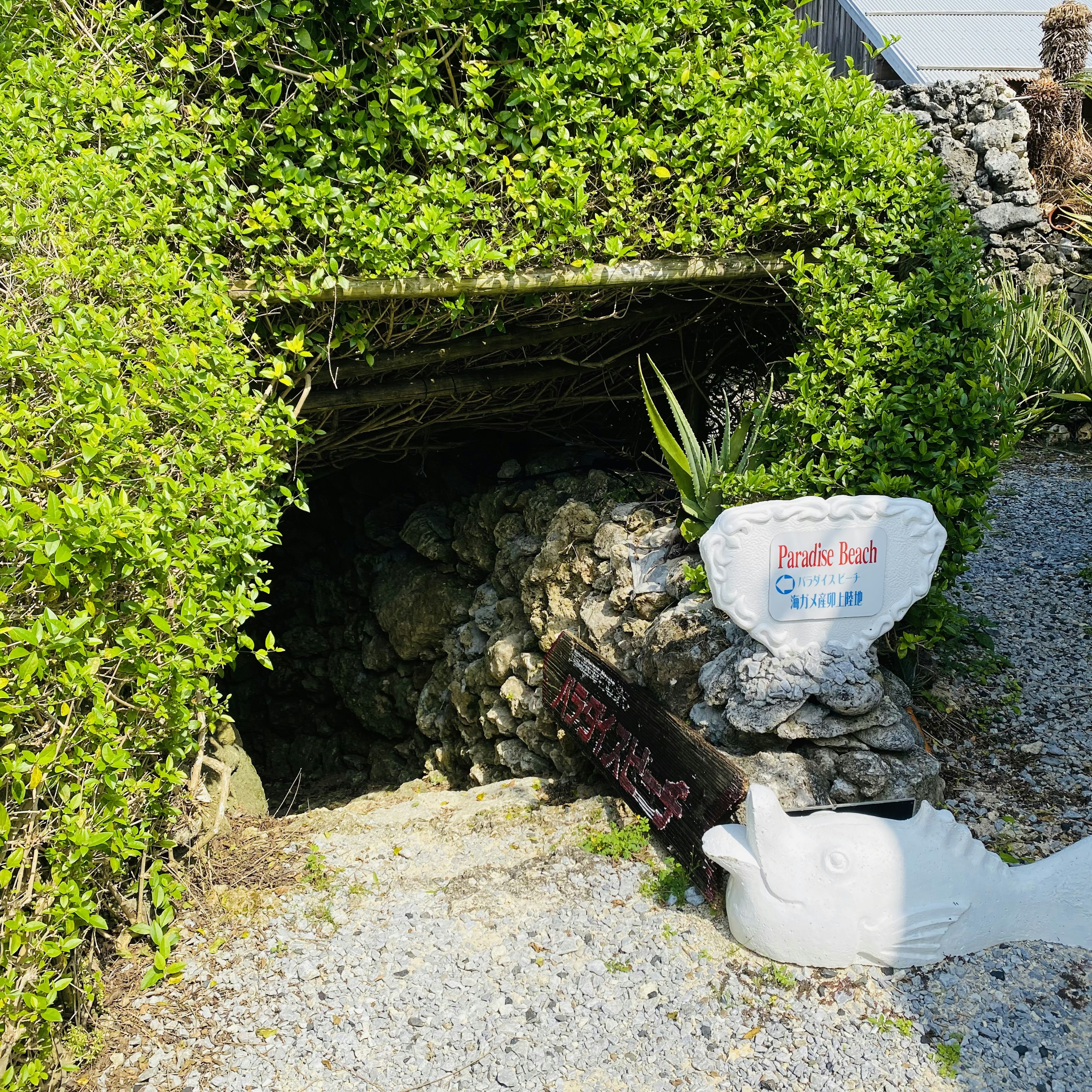 Entrata in pietra circondata da siepi verdi con un cartello