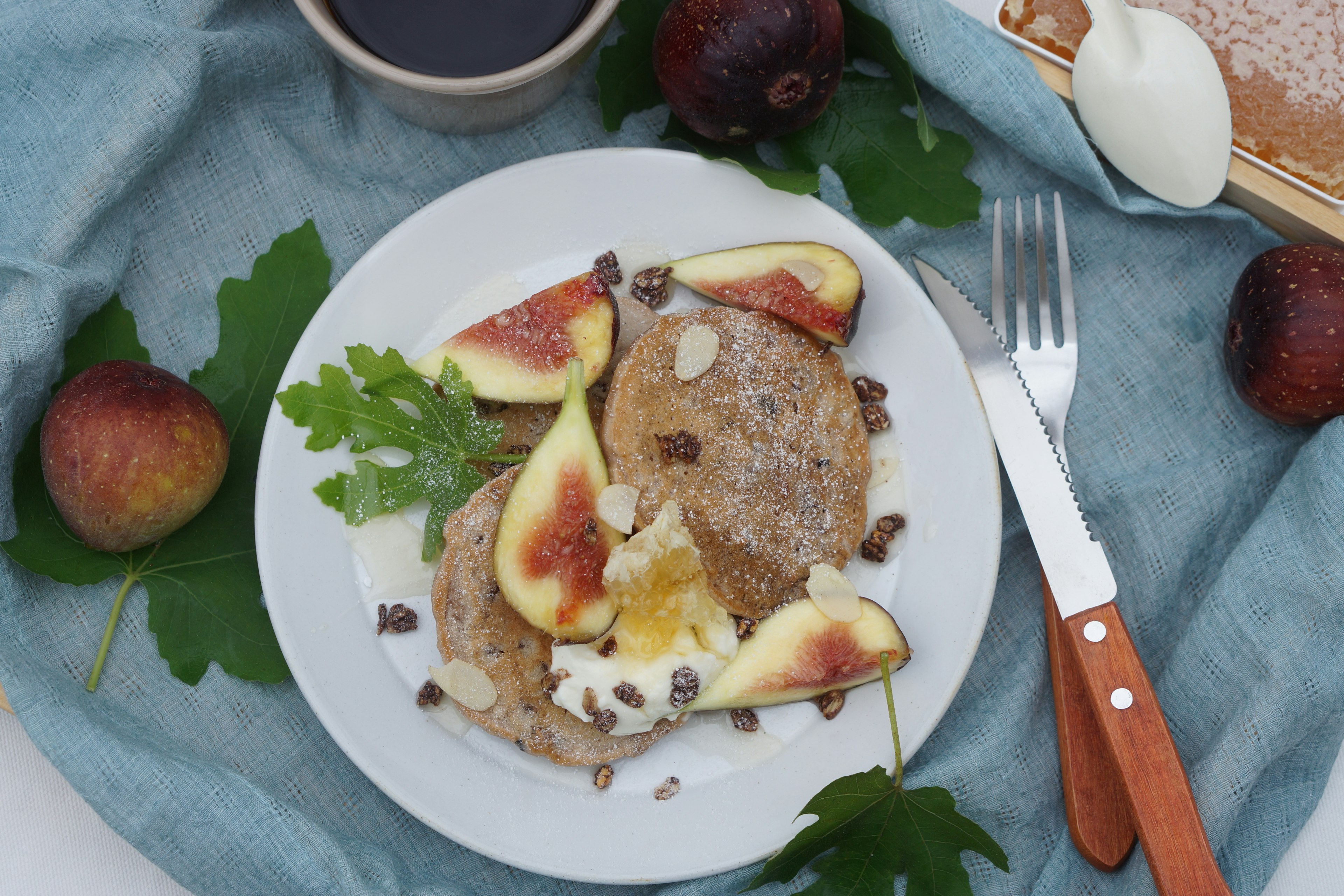 Pancakes garnis de figues fraîches et de crème sur une assiette avec des feuilles vertes et du café