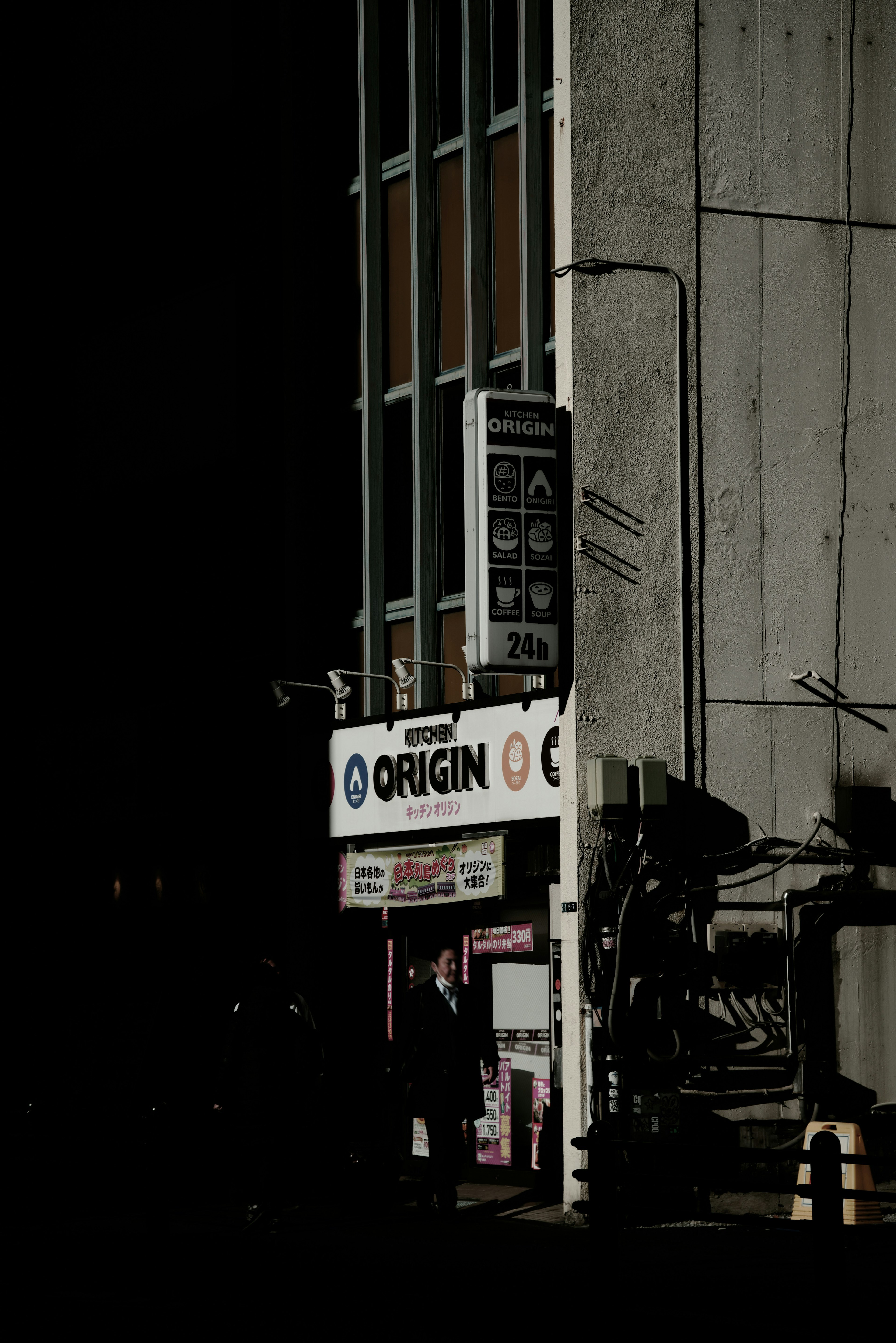 Part of a building with an illuminated sign for Origin against a dark background