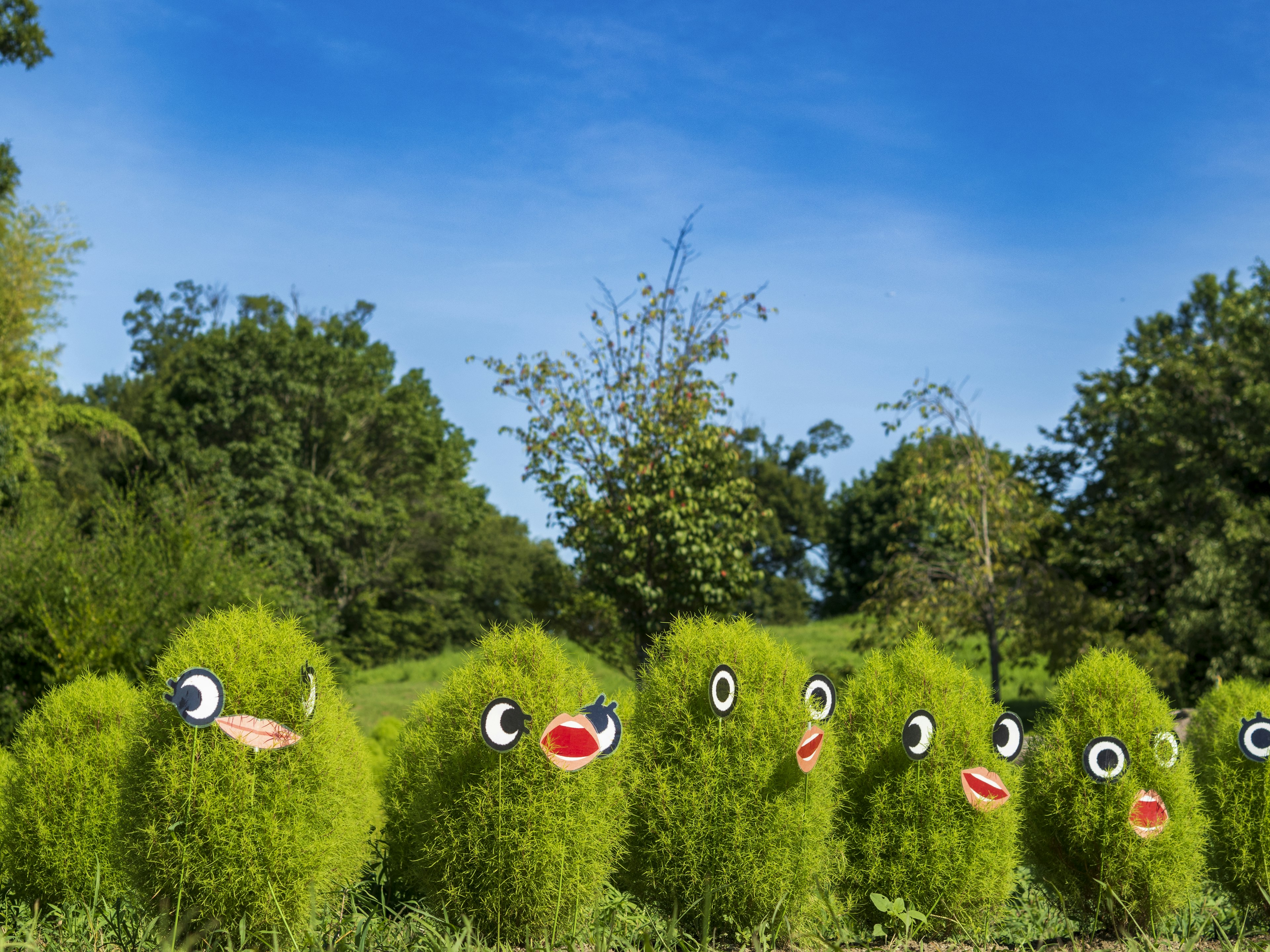 Personajes lindos hechos de hierba verde alineados en un paisaje