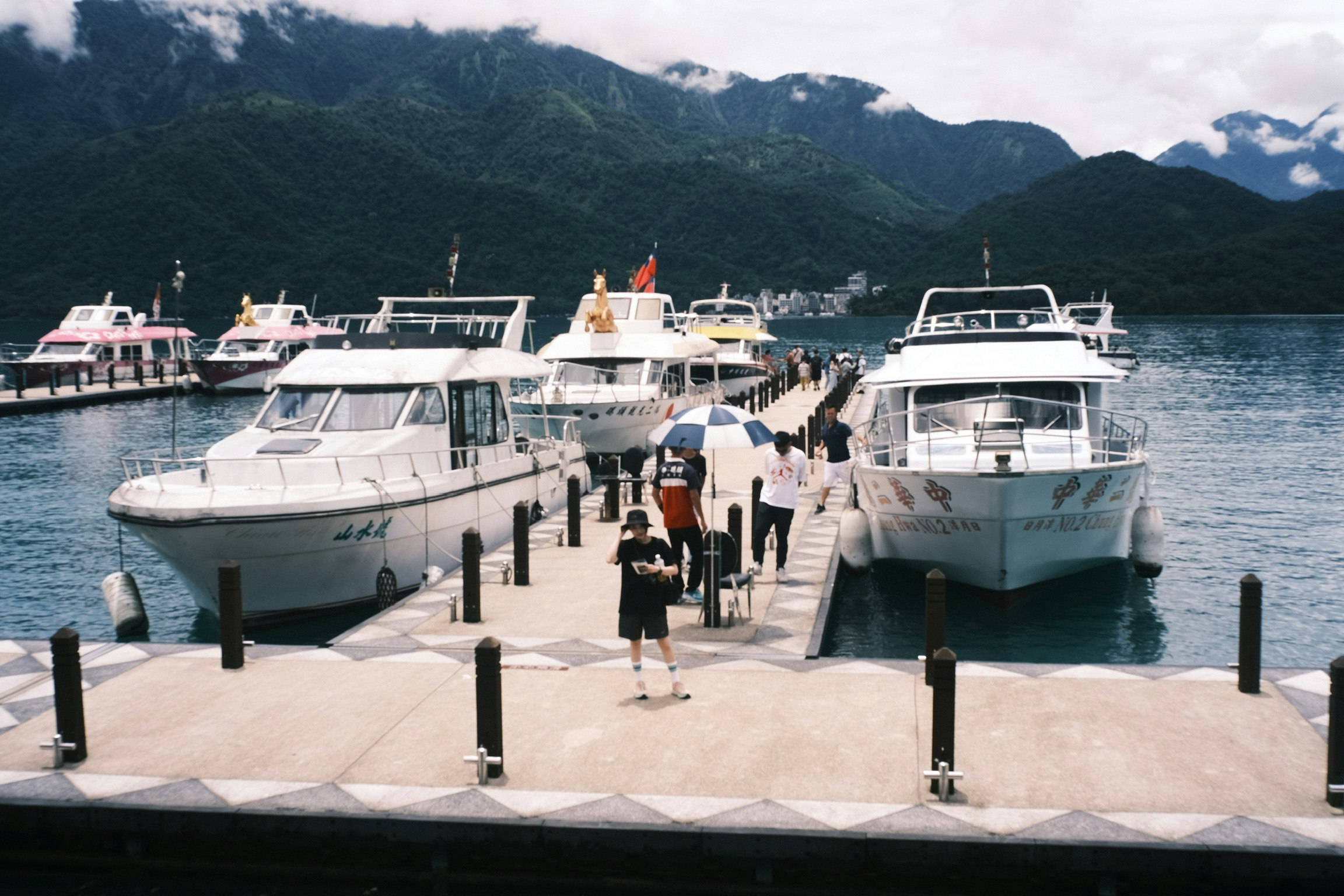 White boats docked at a pier with beautiful mountains in the background and people walking