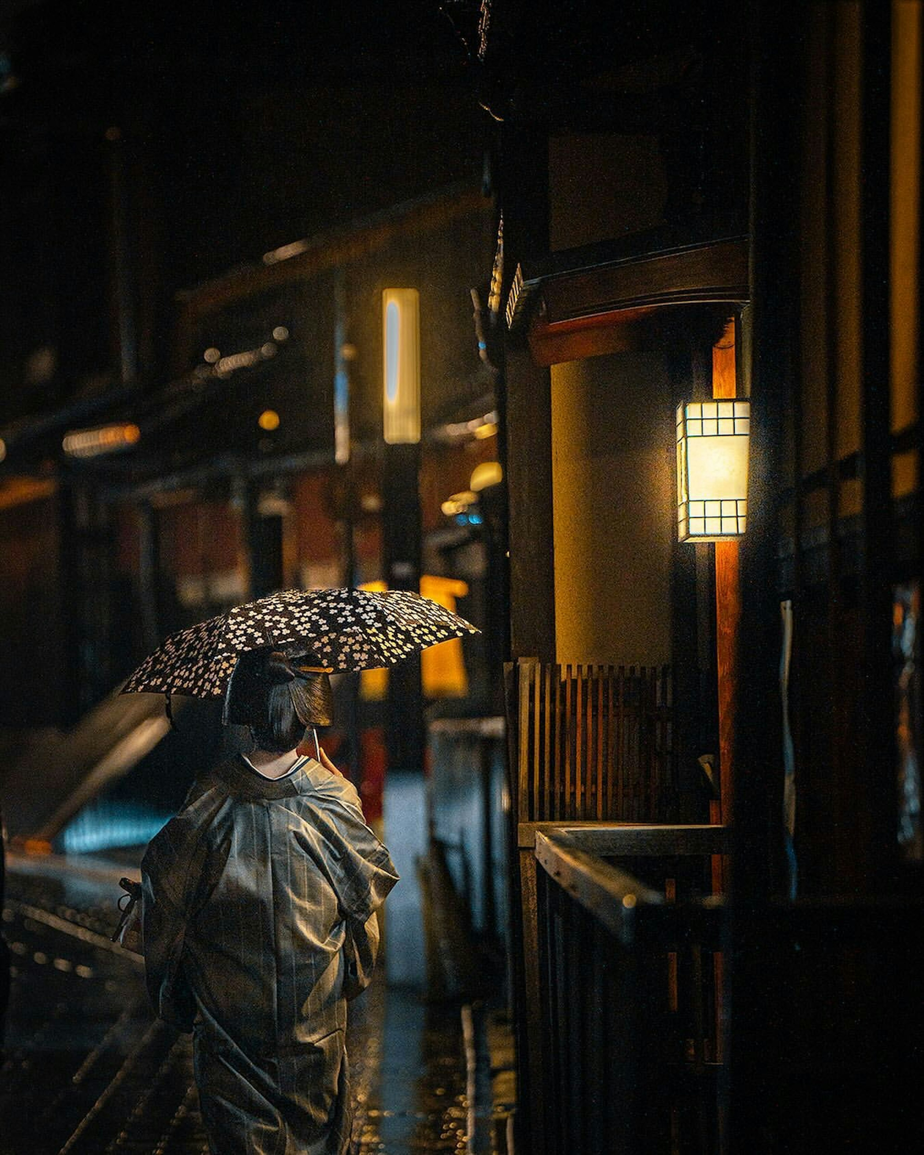 A woman in a kimono walking at night with a traditional umbrella