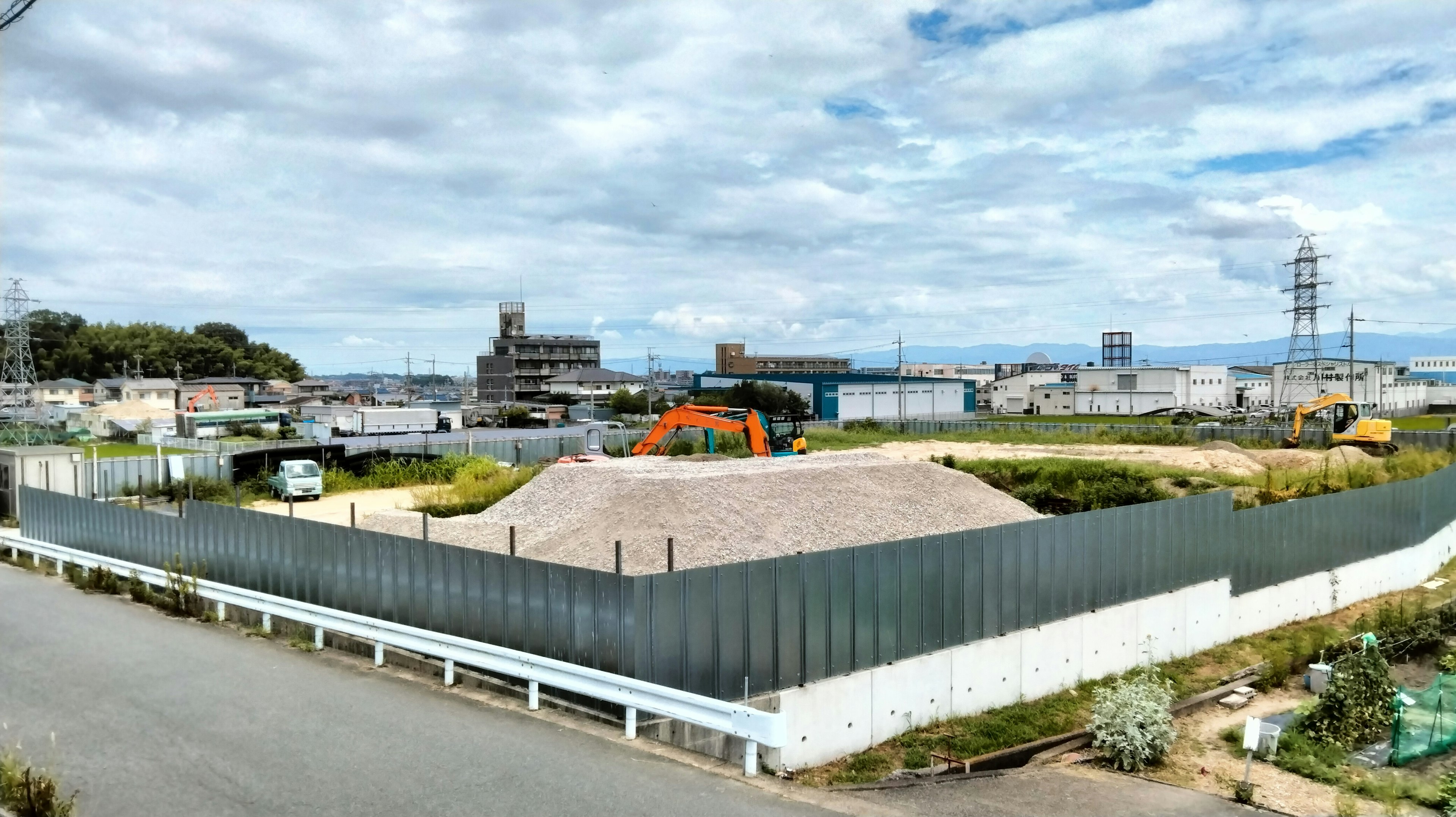 Sitio de construcción con cerca verde y cielo azul rodeando edificios