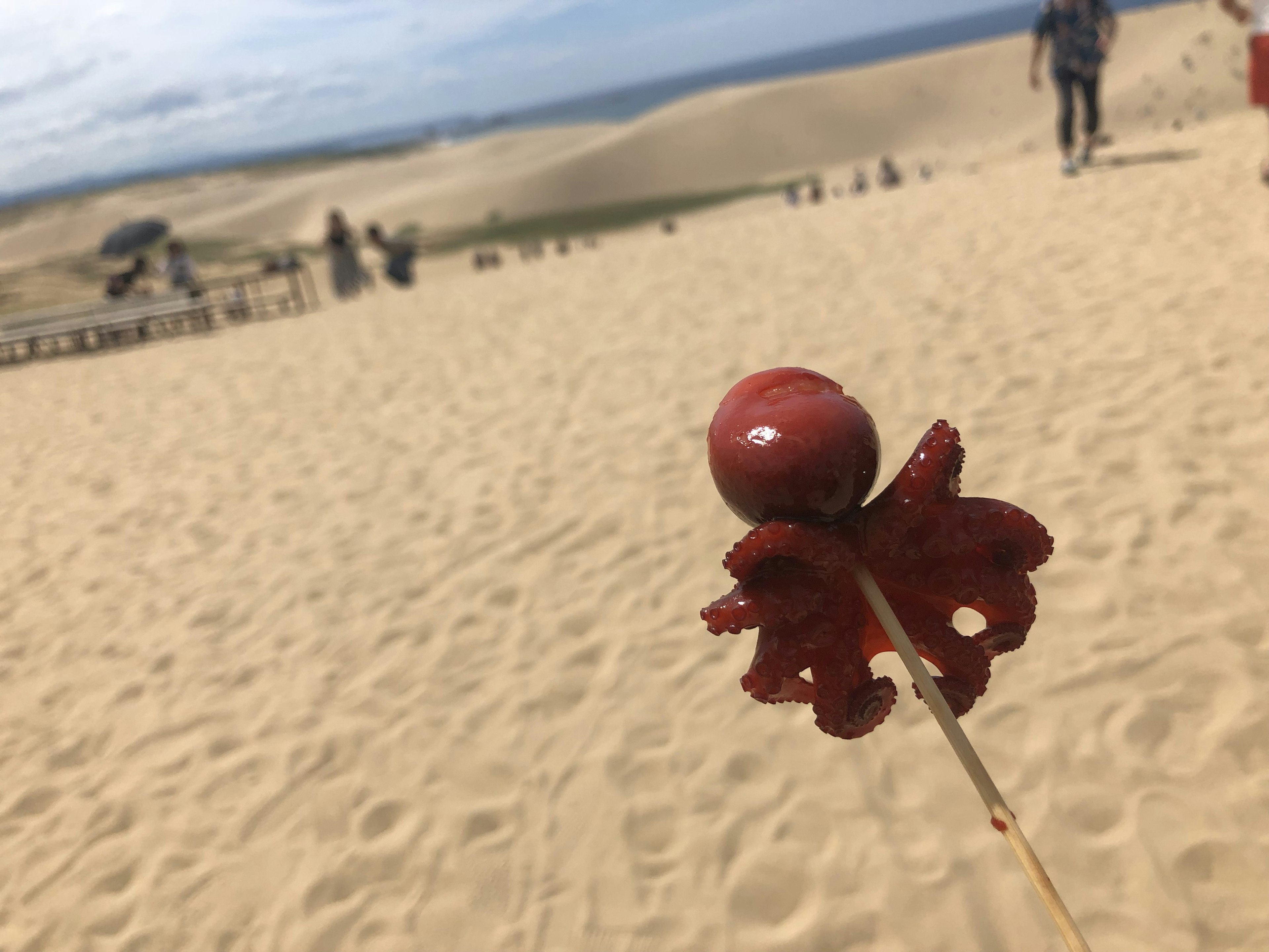 Rote Oktopus-Spieß in einer sandigen Dünenlandschaft mit Menschen im Hintergrund