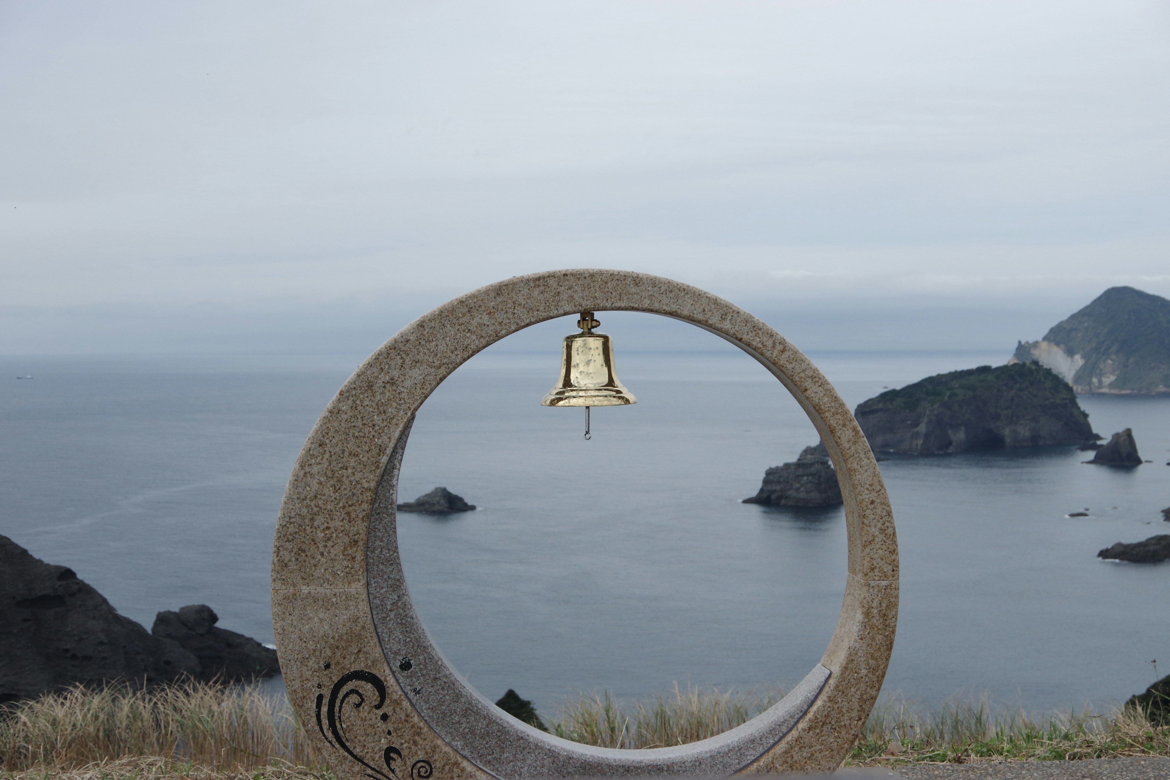 Campana colgante en un marco de piedra con vista al océano