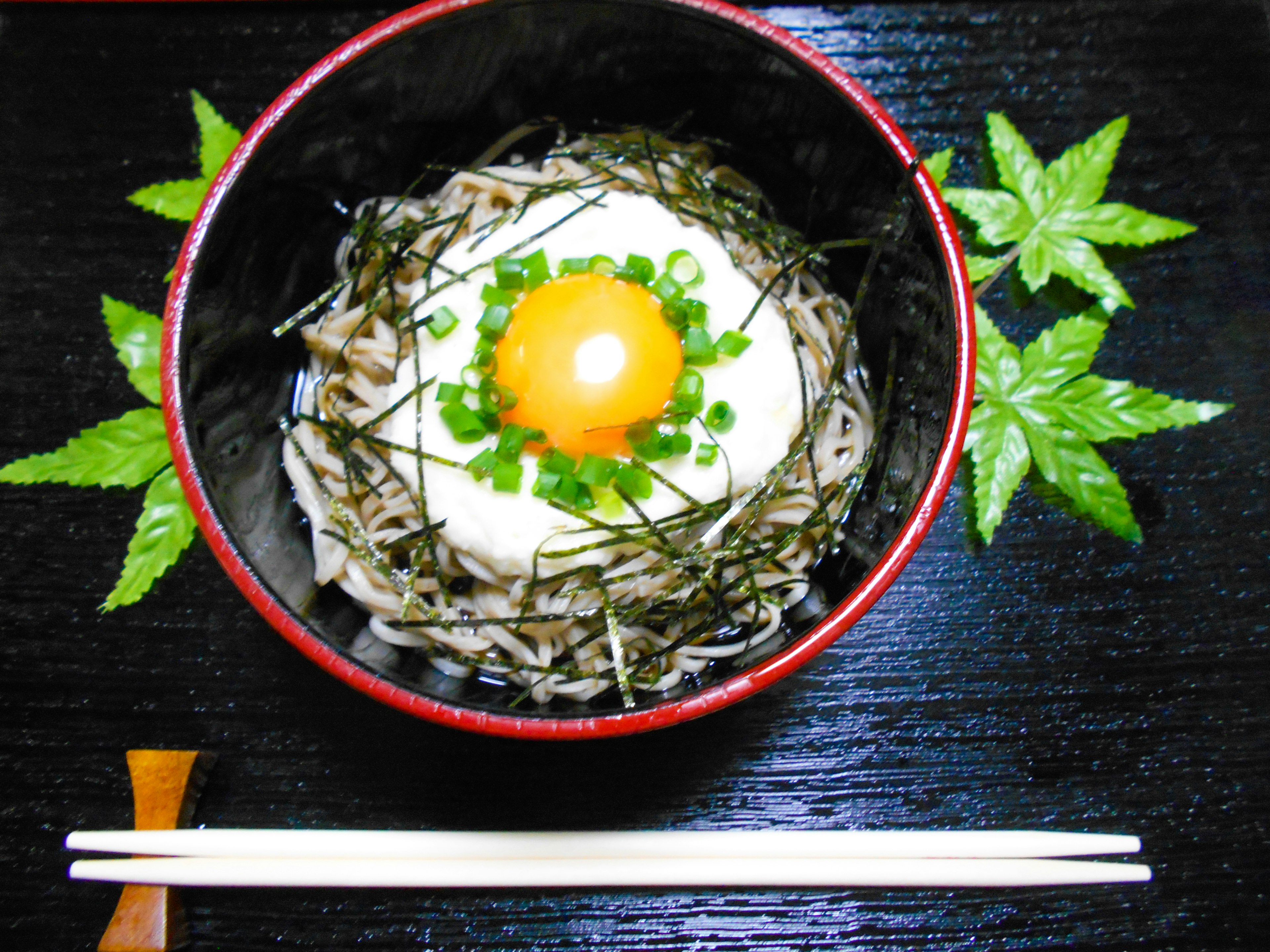 Japanese noodle dish topped with egg yolk and green onions served in a red bowl