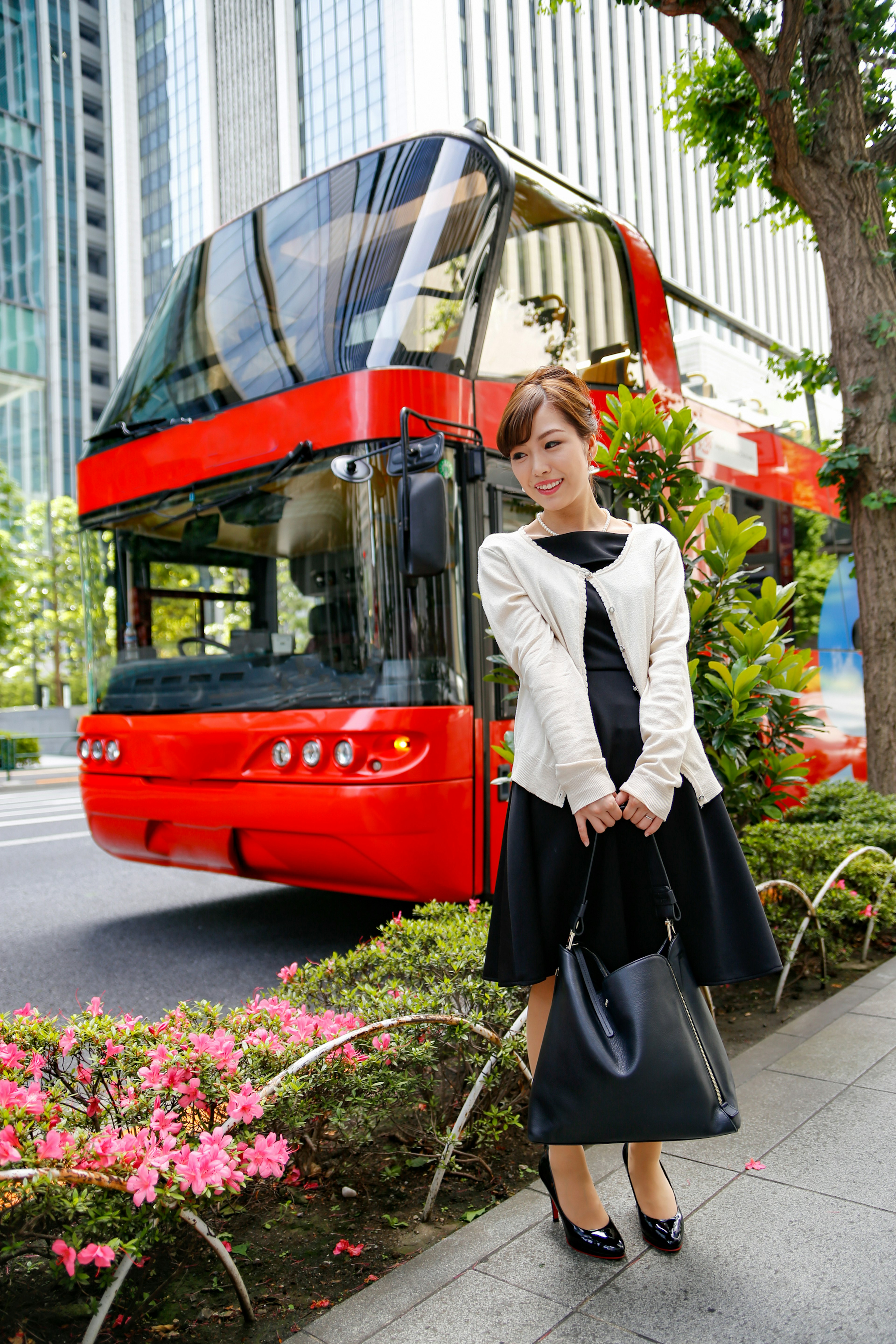 A woman standing in front of a red bus with plants and flowers around in an urban setting