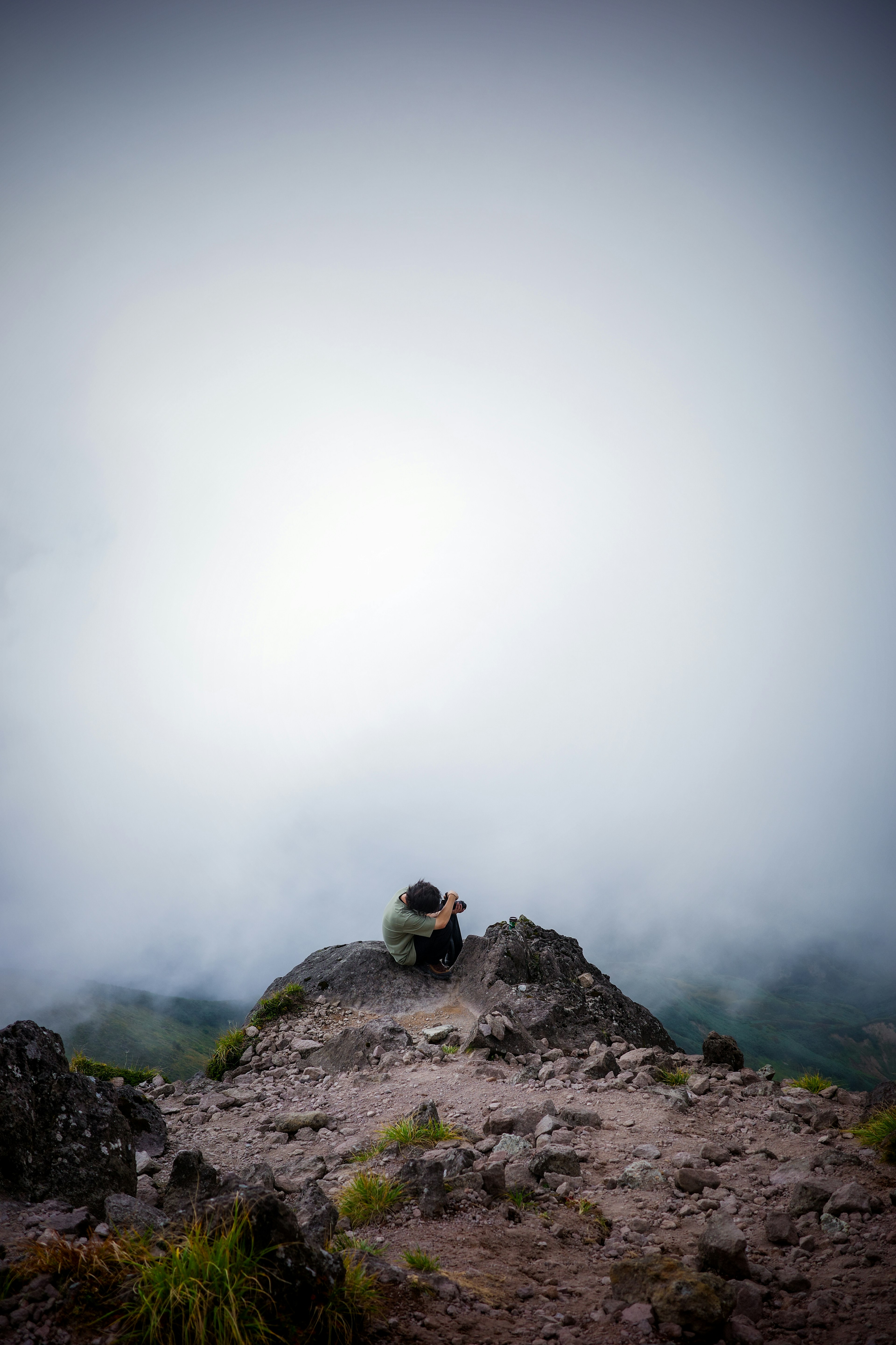 Orang duduk di puncak gunung dikelilingi kabut