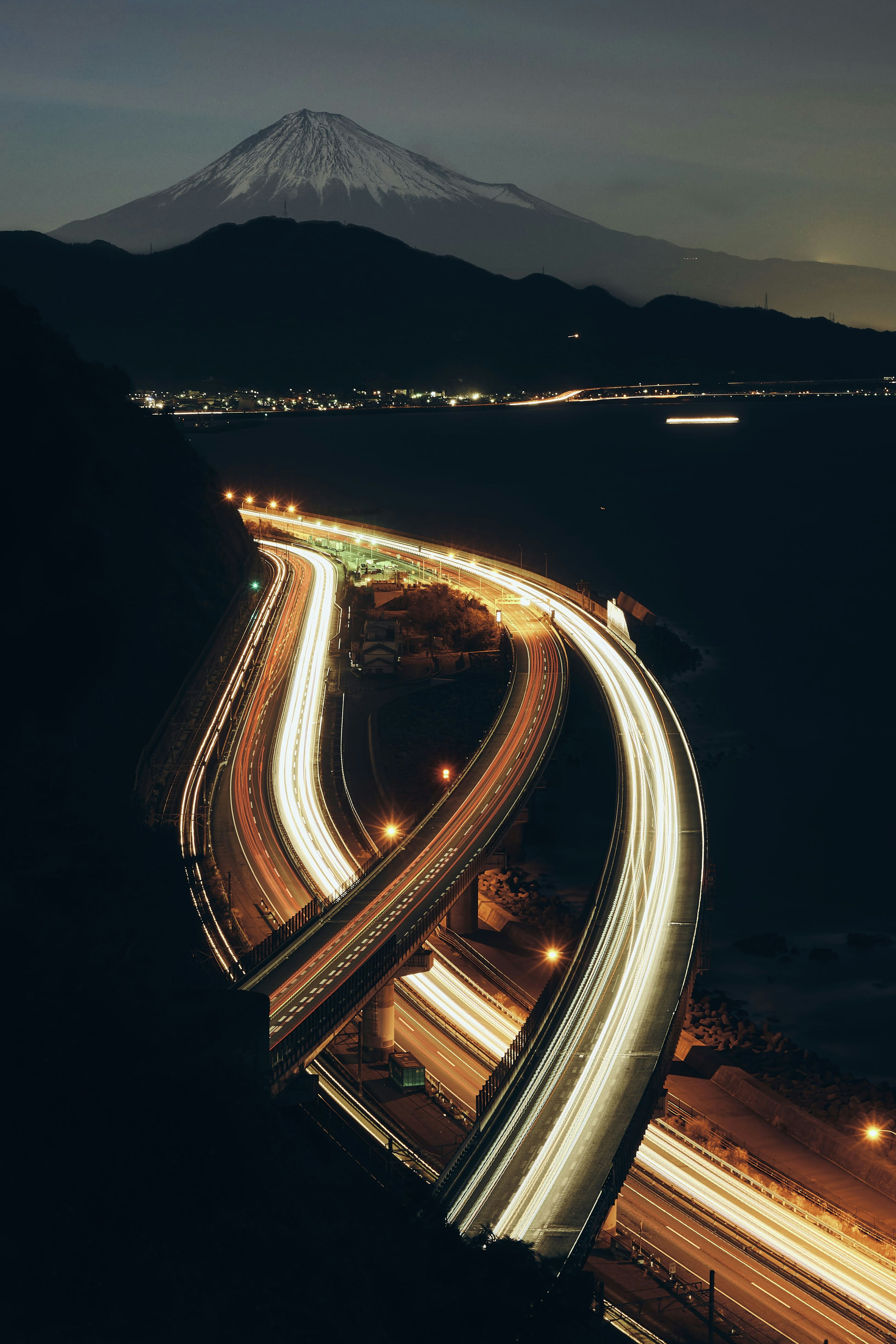 Autostrada curva con scie di luce e il monte Fuji sullo sfondo di notte