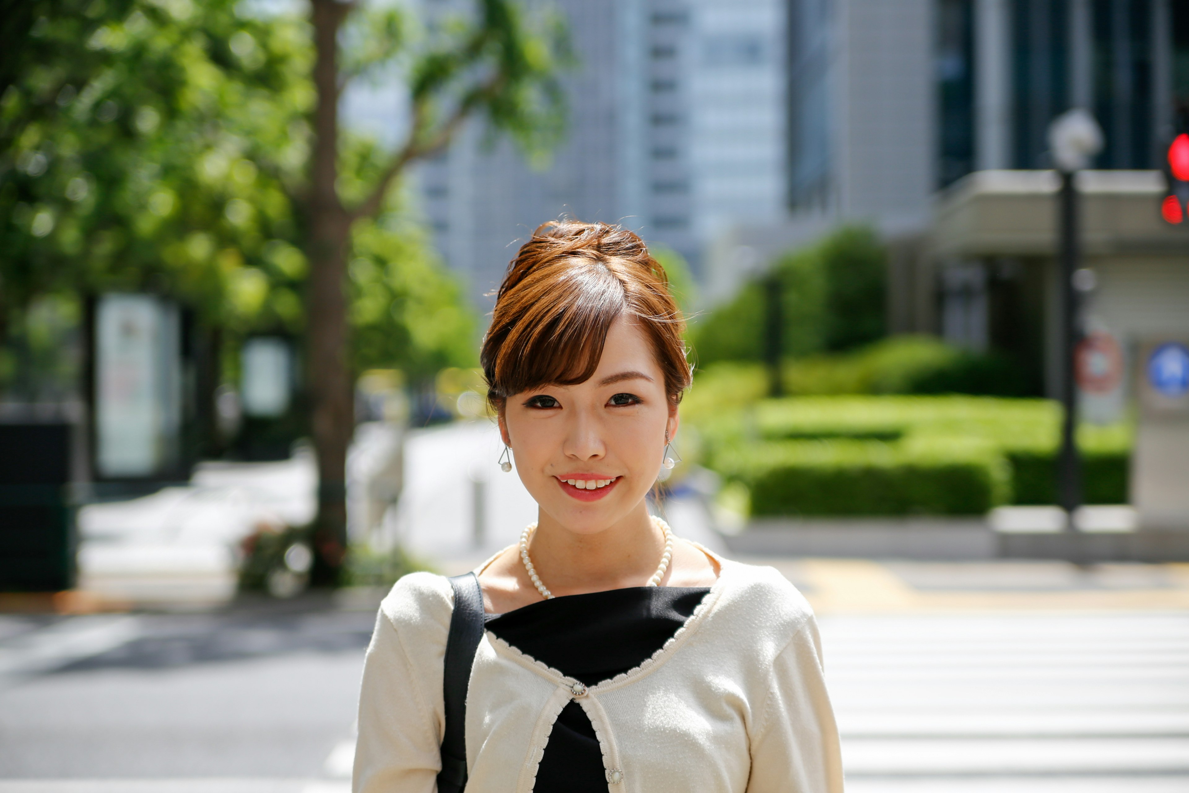 Portrait of a smiling woman on a city street with green trees and buildings in the background