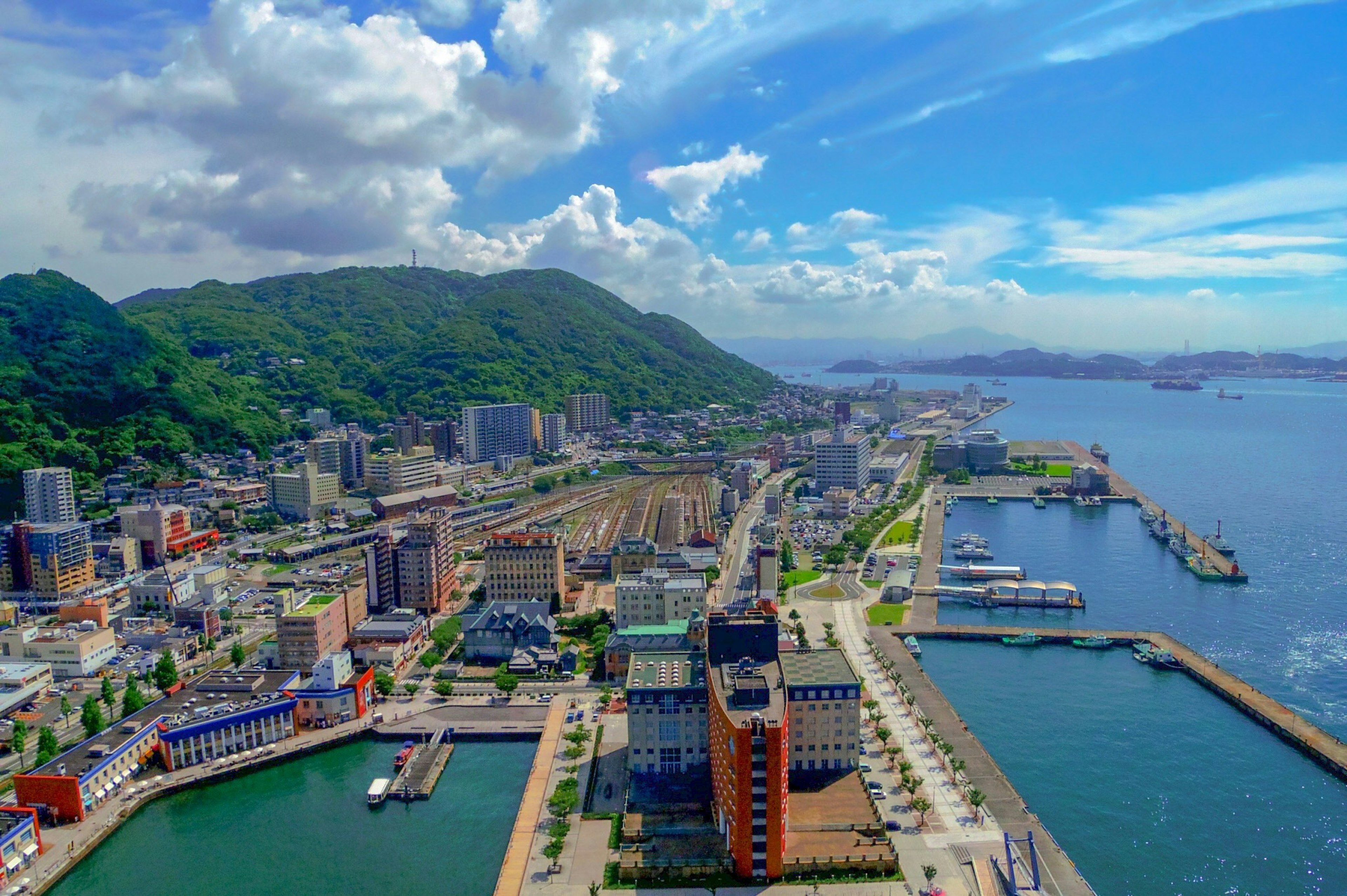 Aerial view of a vibrant port city with lush green mountains and a blue sky