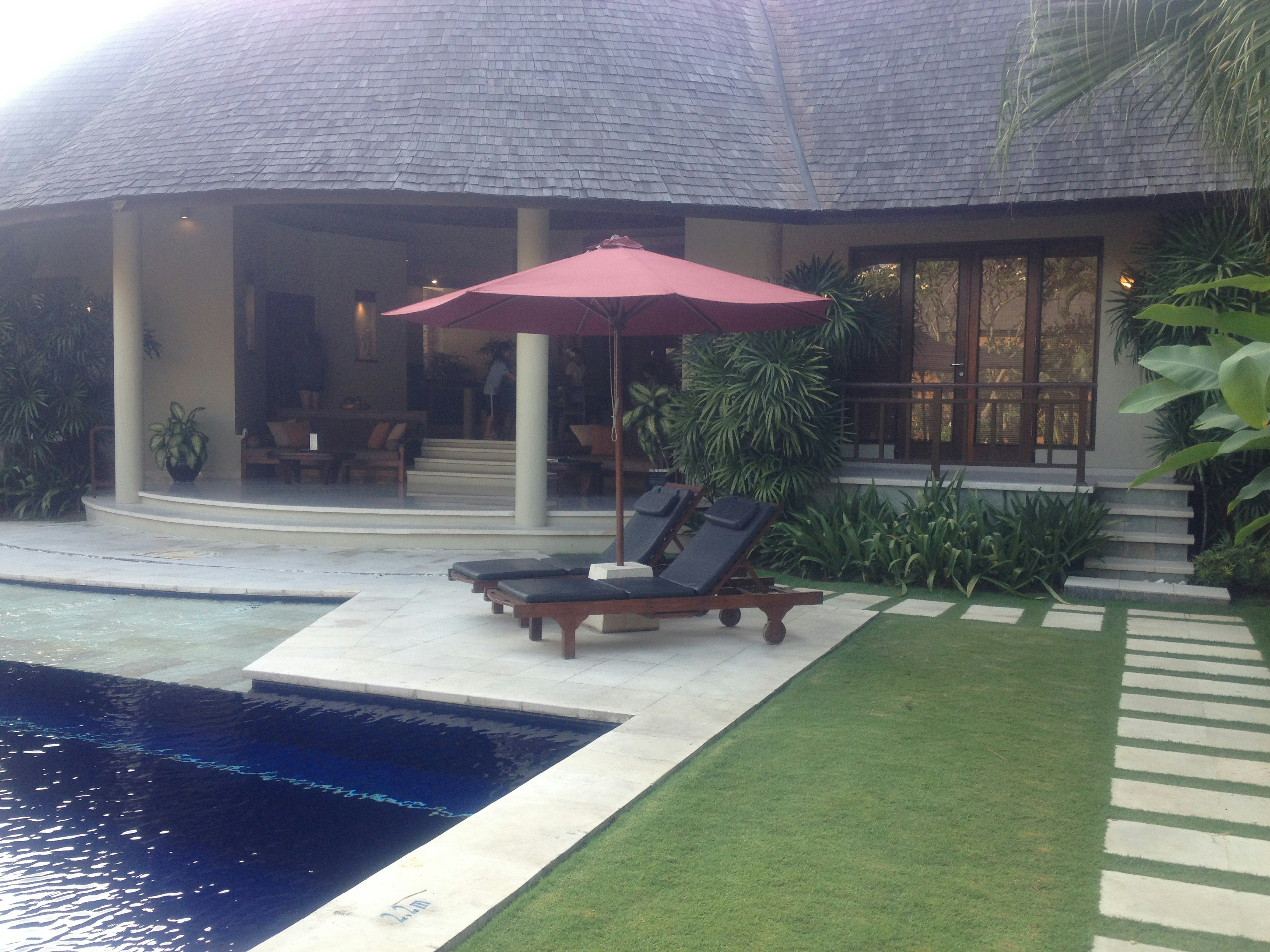 Hermosa casa con una tumbona junto a la piscina y una sombrilla roja en un jardín