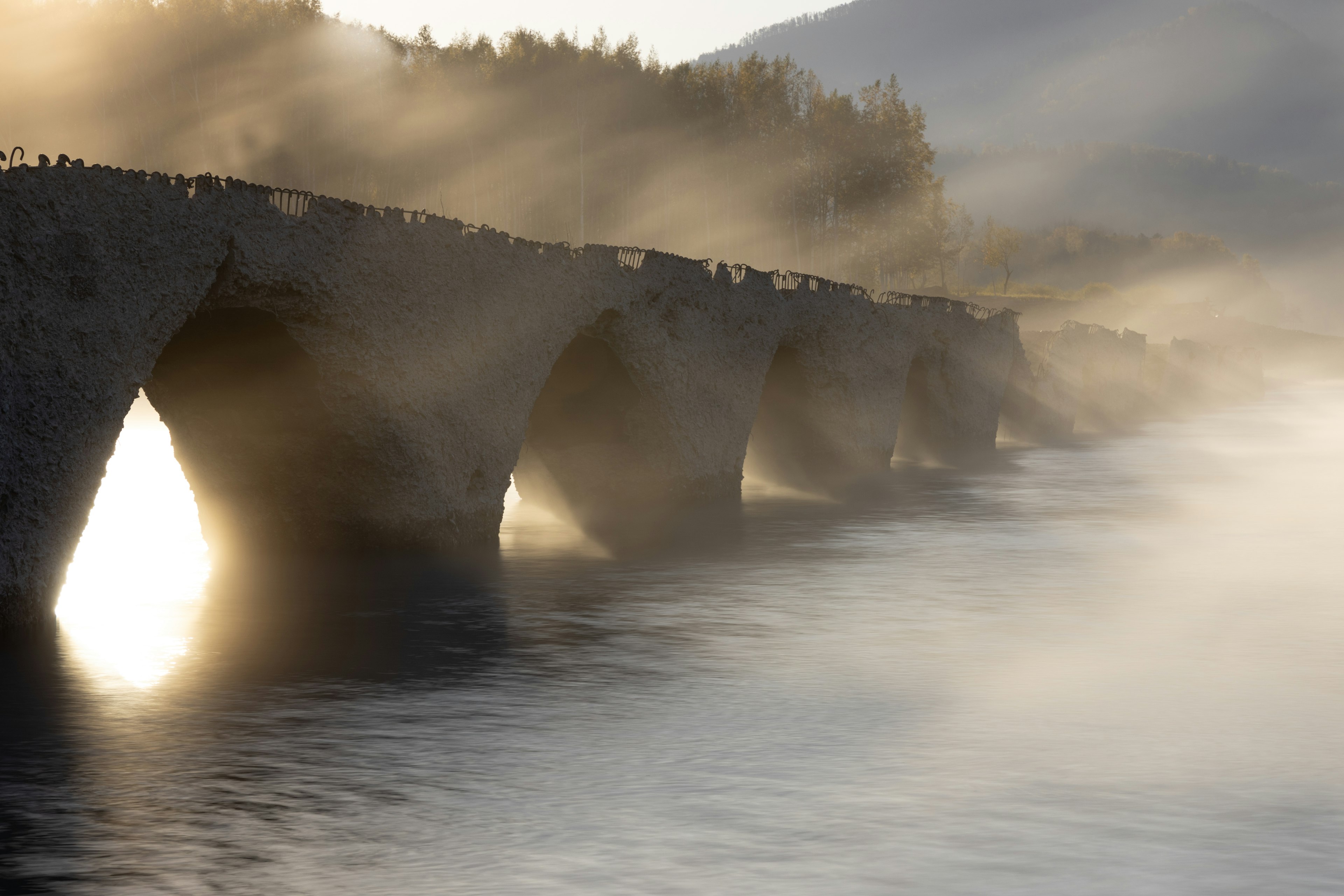 Puente de piedra antiguo envuelto en niebla con agua tranquila abajo