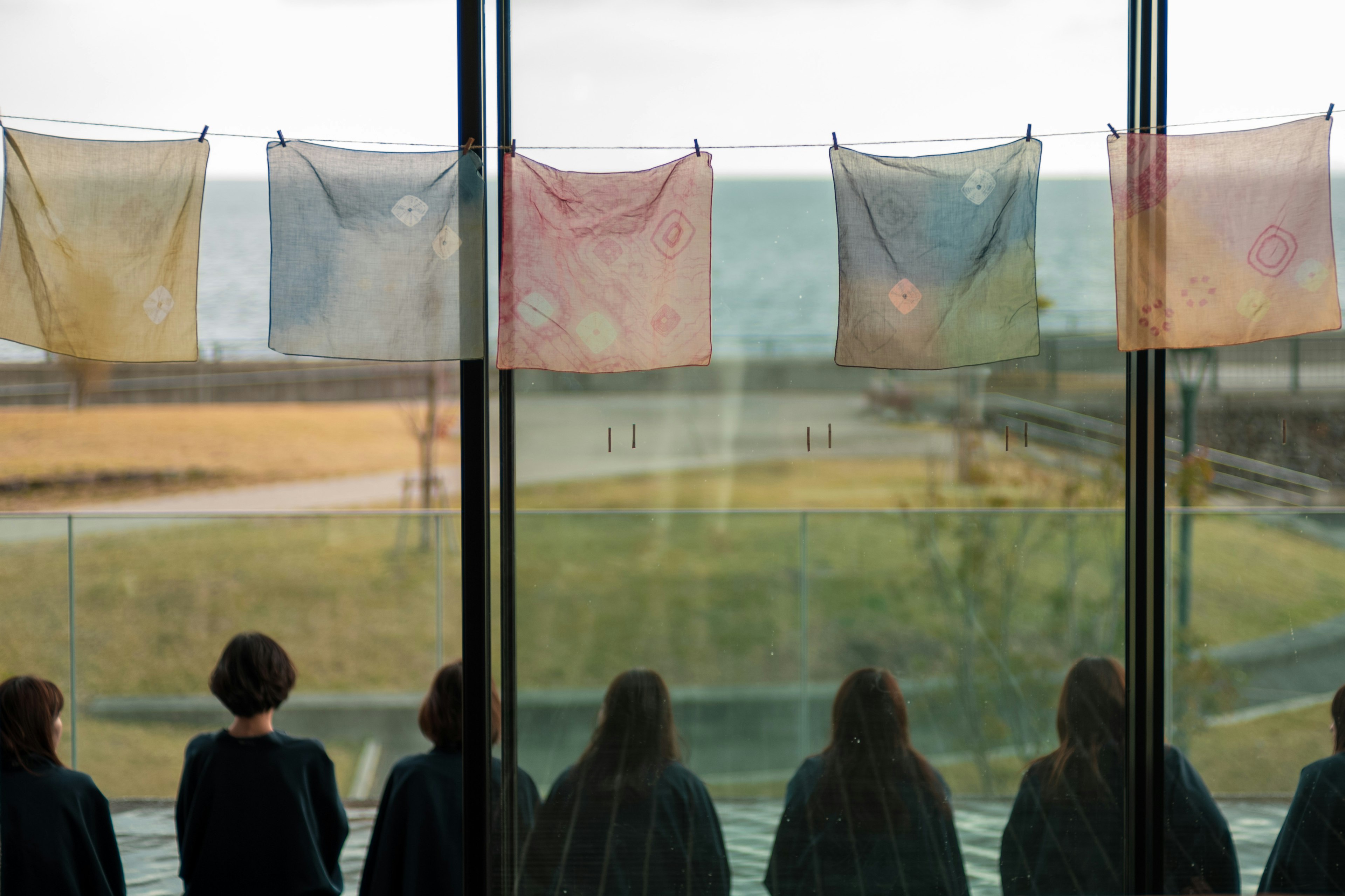 Silhouetten von Personen an einem Fenster mit bunten Stoffen vor einer Meereskulisse