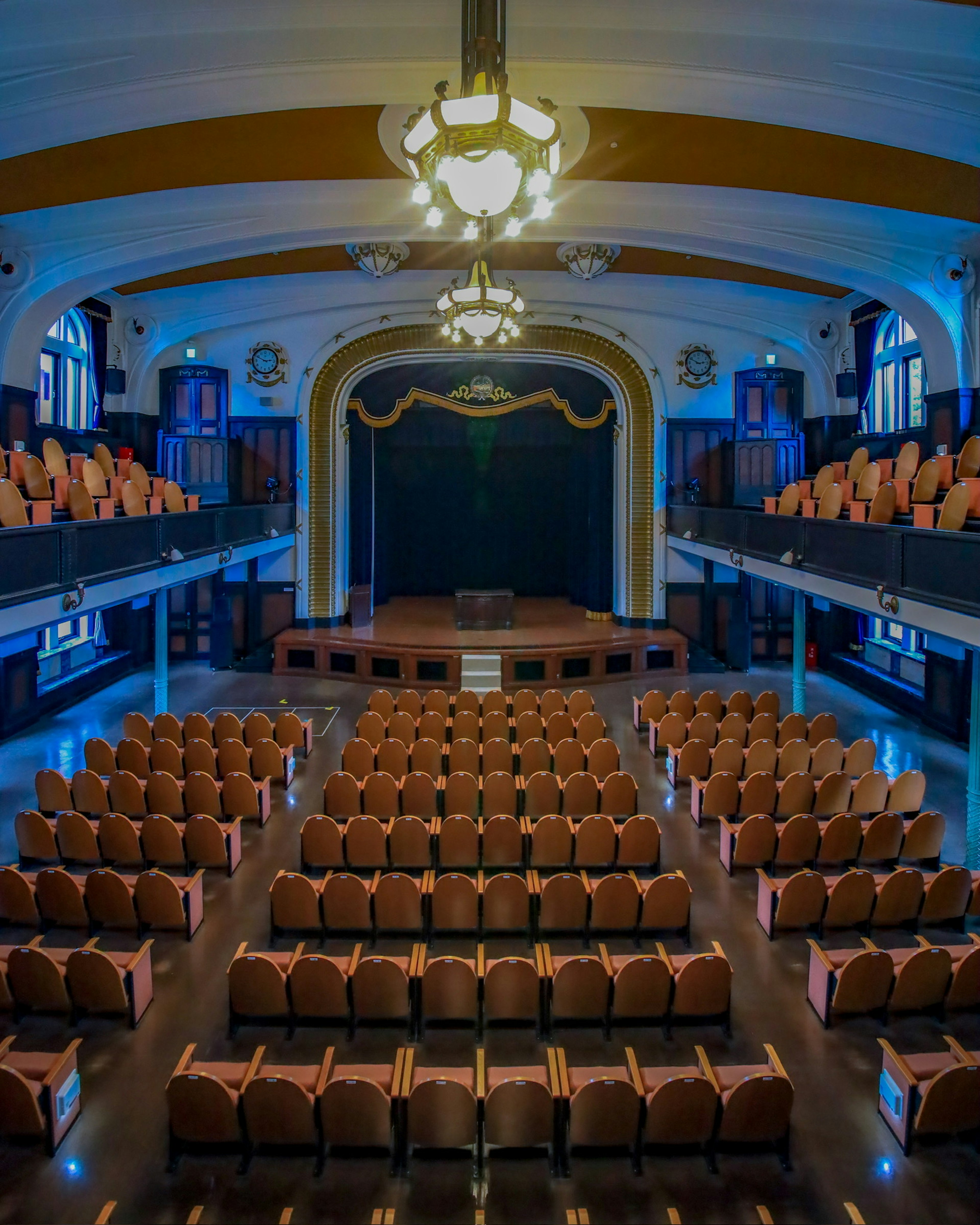 Intérieur d'un théâtre avec un éclairage bleu rangées de sièges disposées et une scène visible