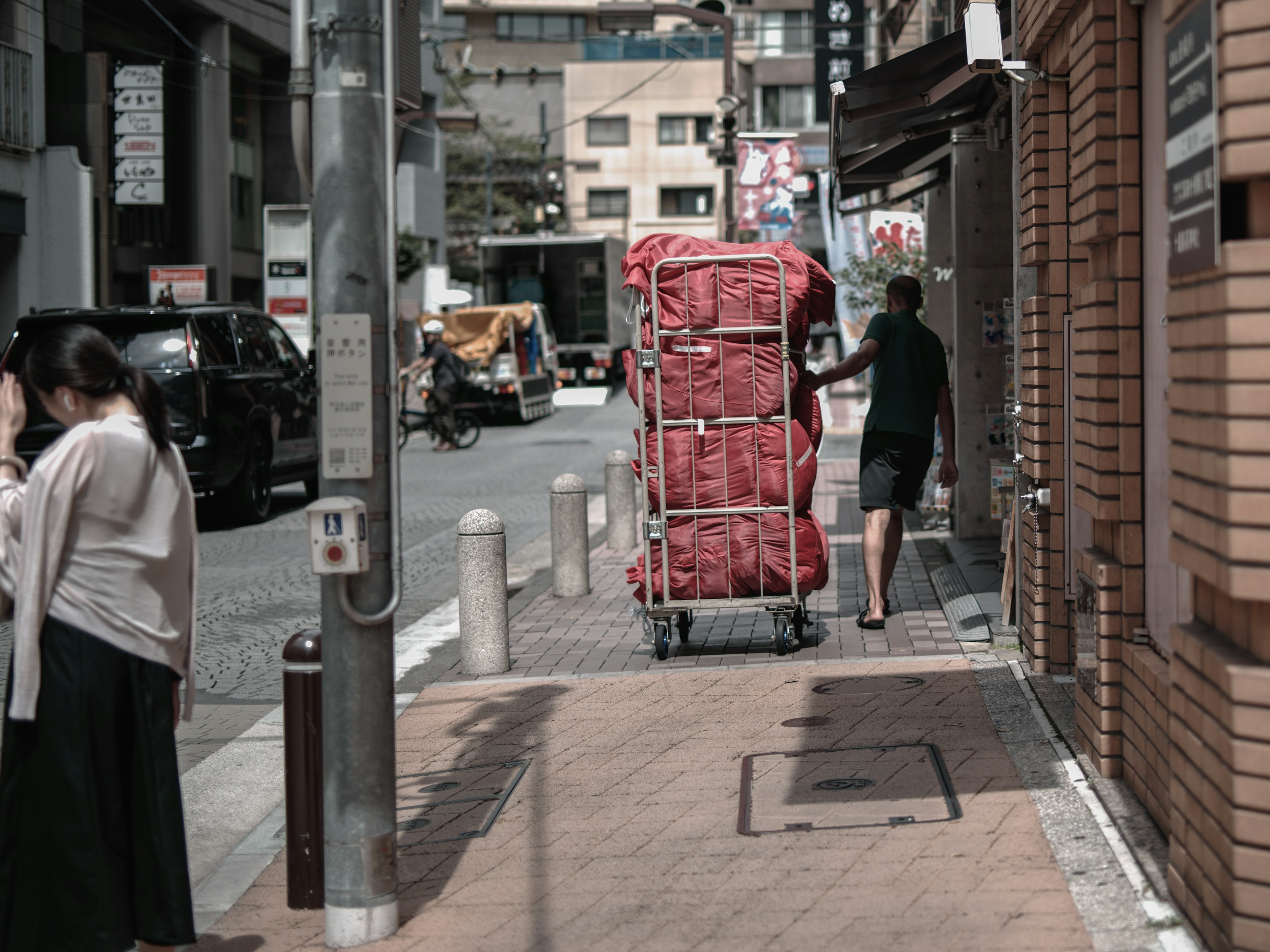 一个人在城市街道上推着红色手推车，旁边有行人