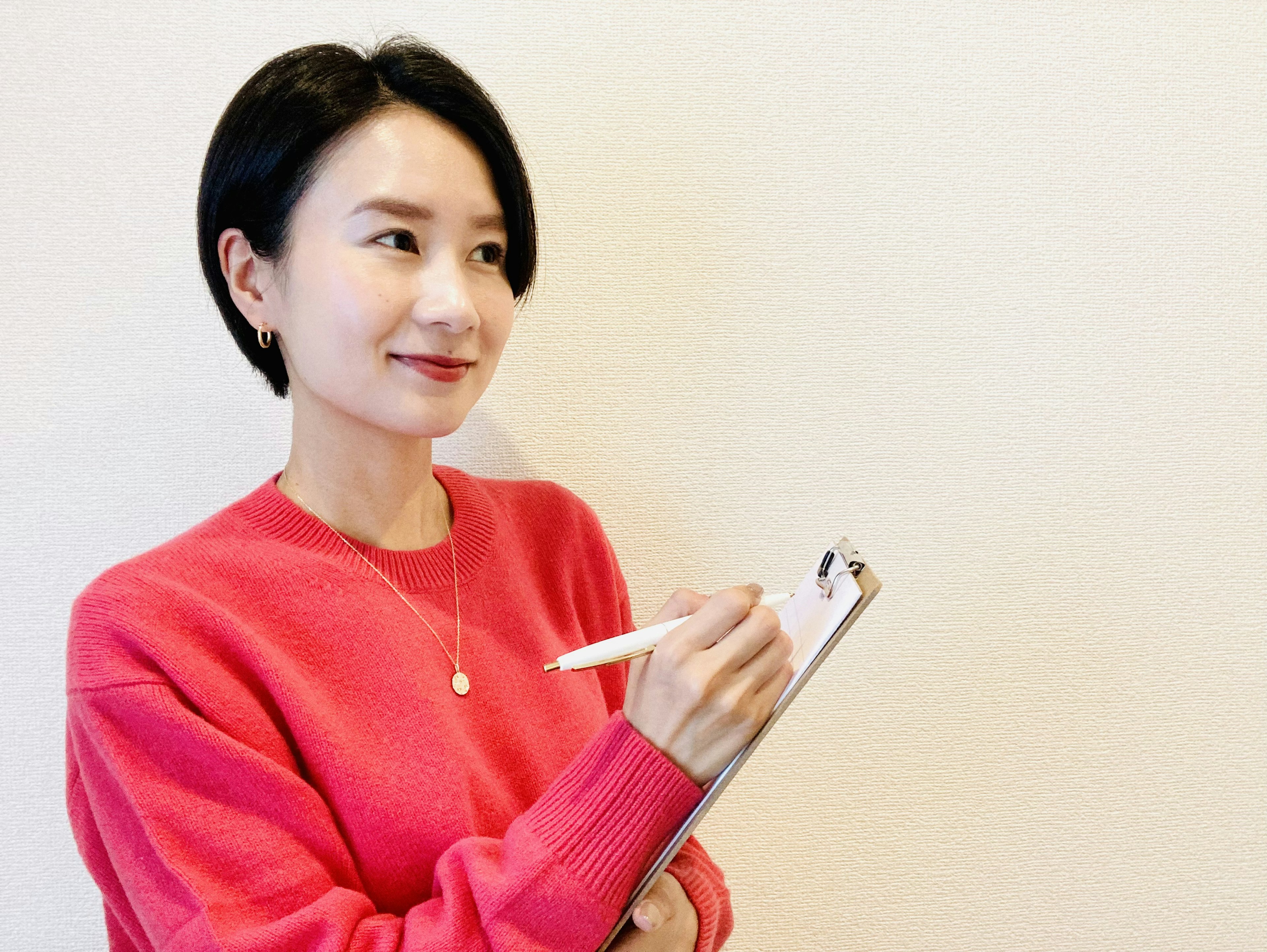 Woman in a pink sweater holding a clipboard and pen