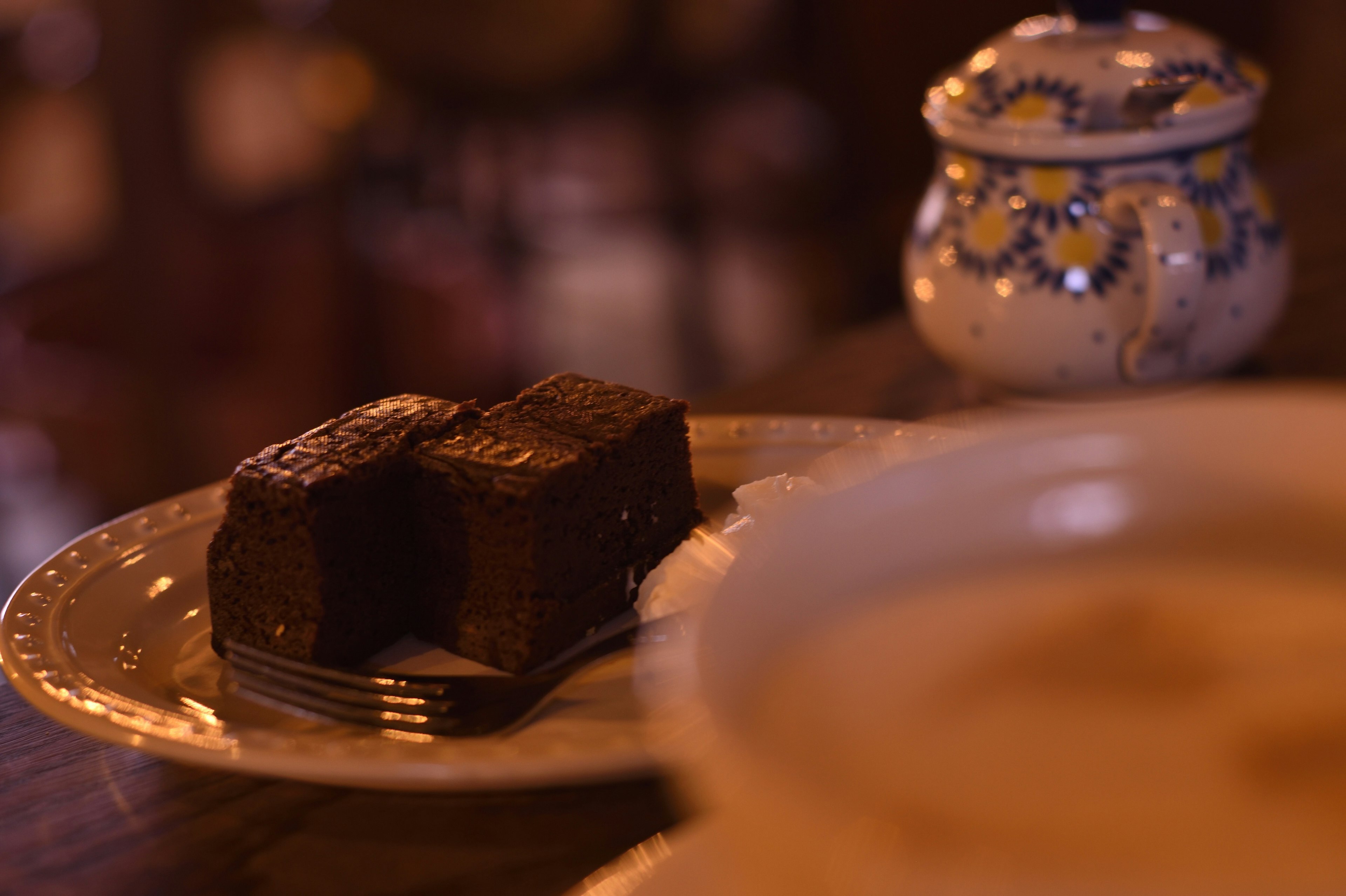 Two pieces of chocolate on a plate with a white dish and a decorative sugar bowl