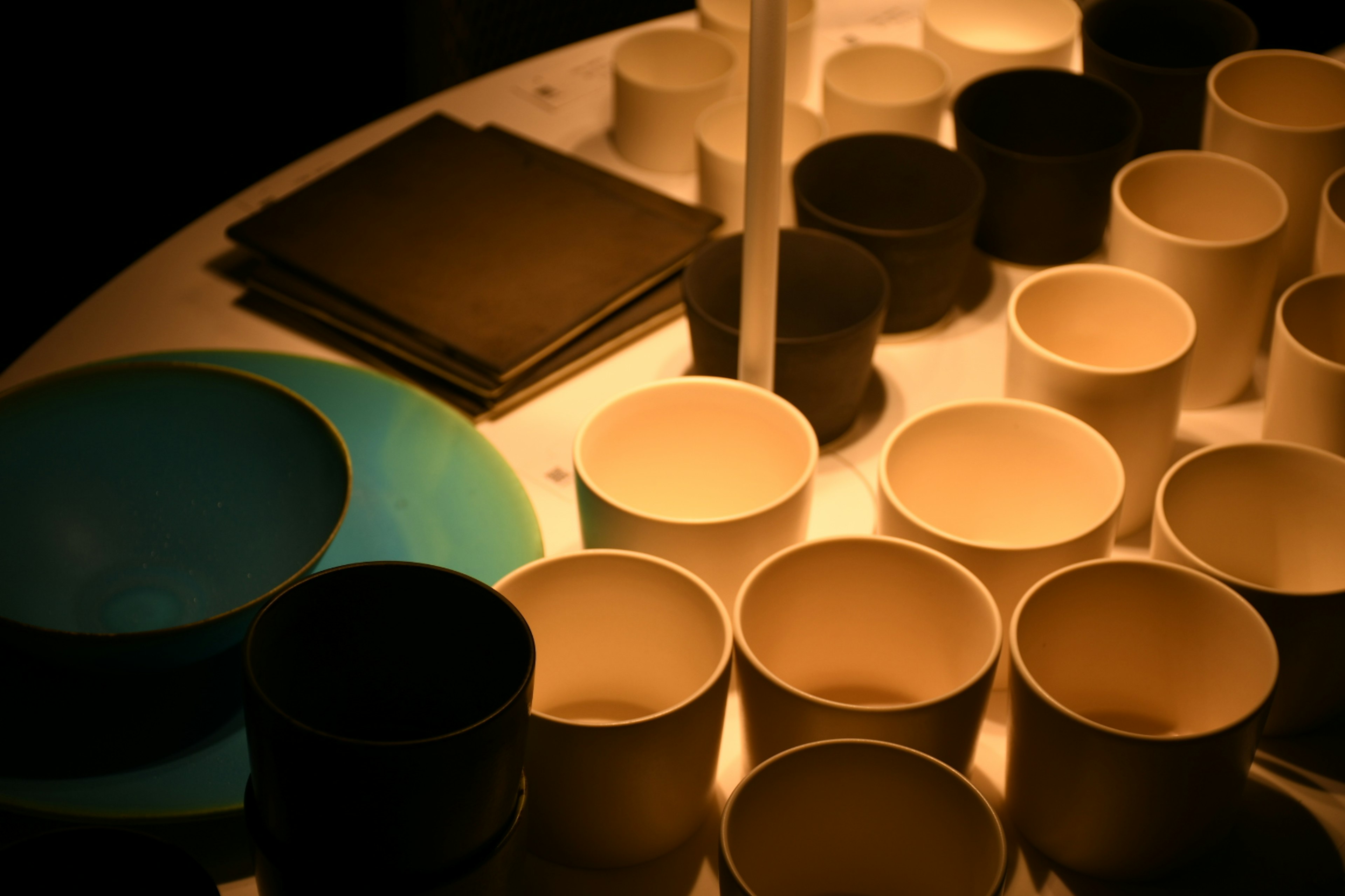 Arrangement of white and black cups with a blue plate on a table illuminated by soft light