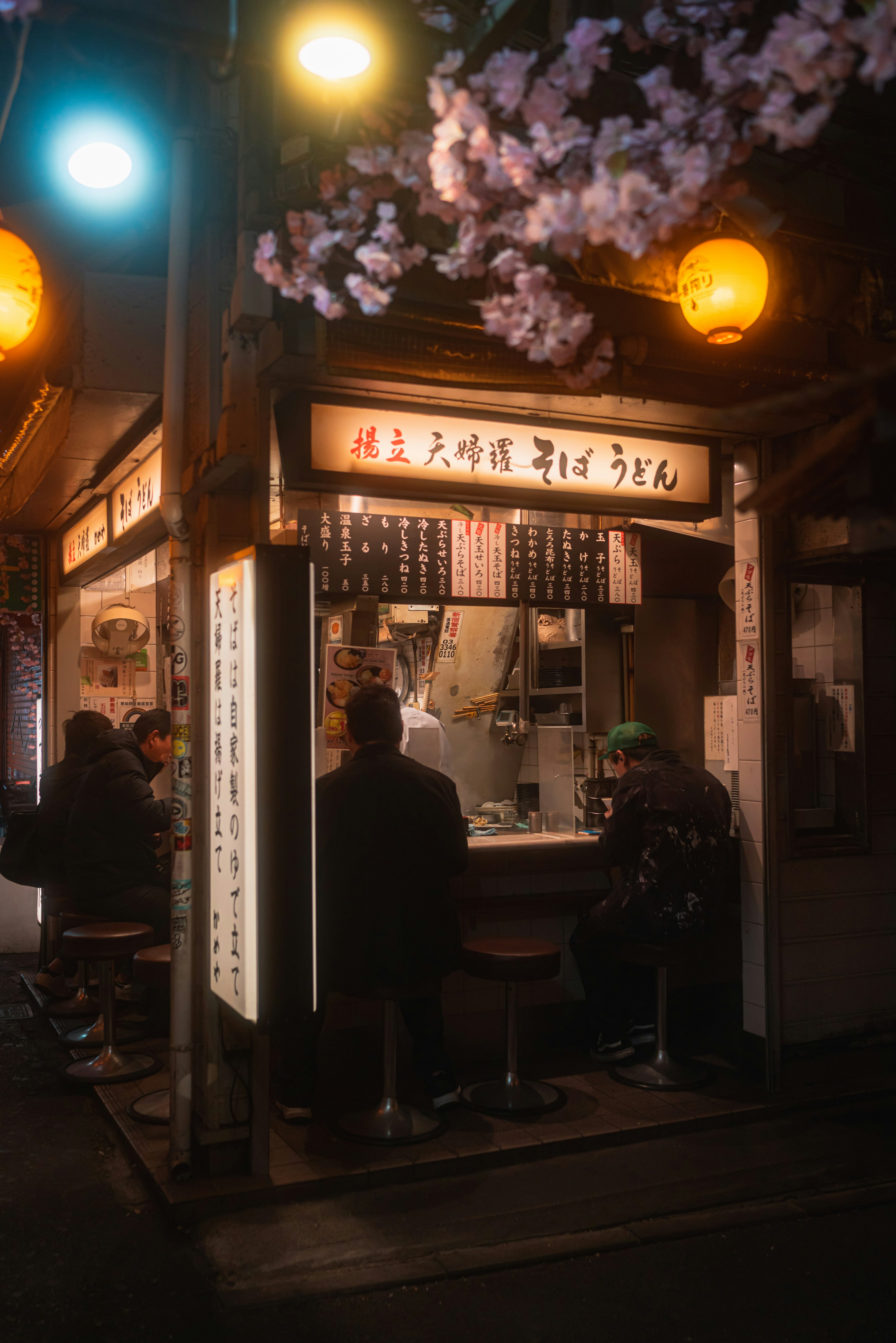 夜の桜と提灯が飾られた小さな食堂で人々が食事を楽しんでいる