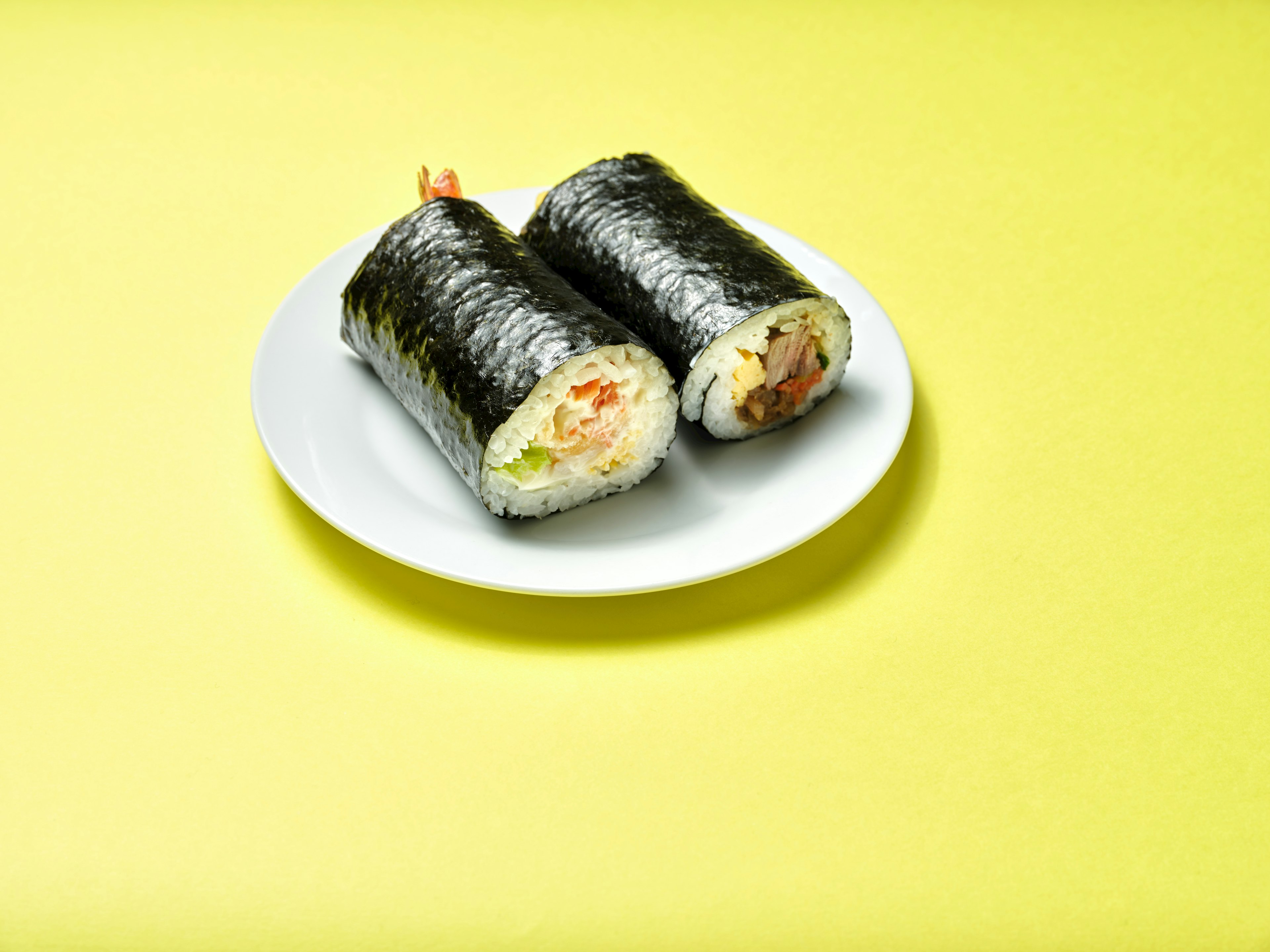 Zwei Sushi-Rollen auf einem weißen Teller mit gelbem Hintergrund