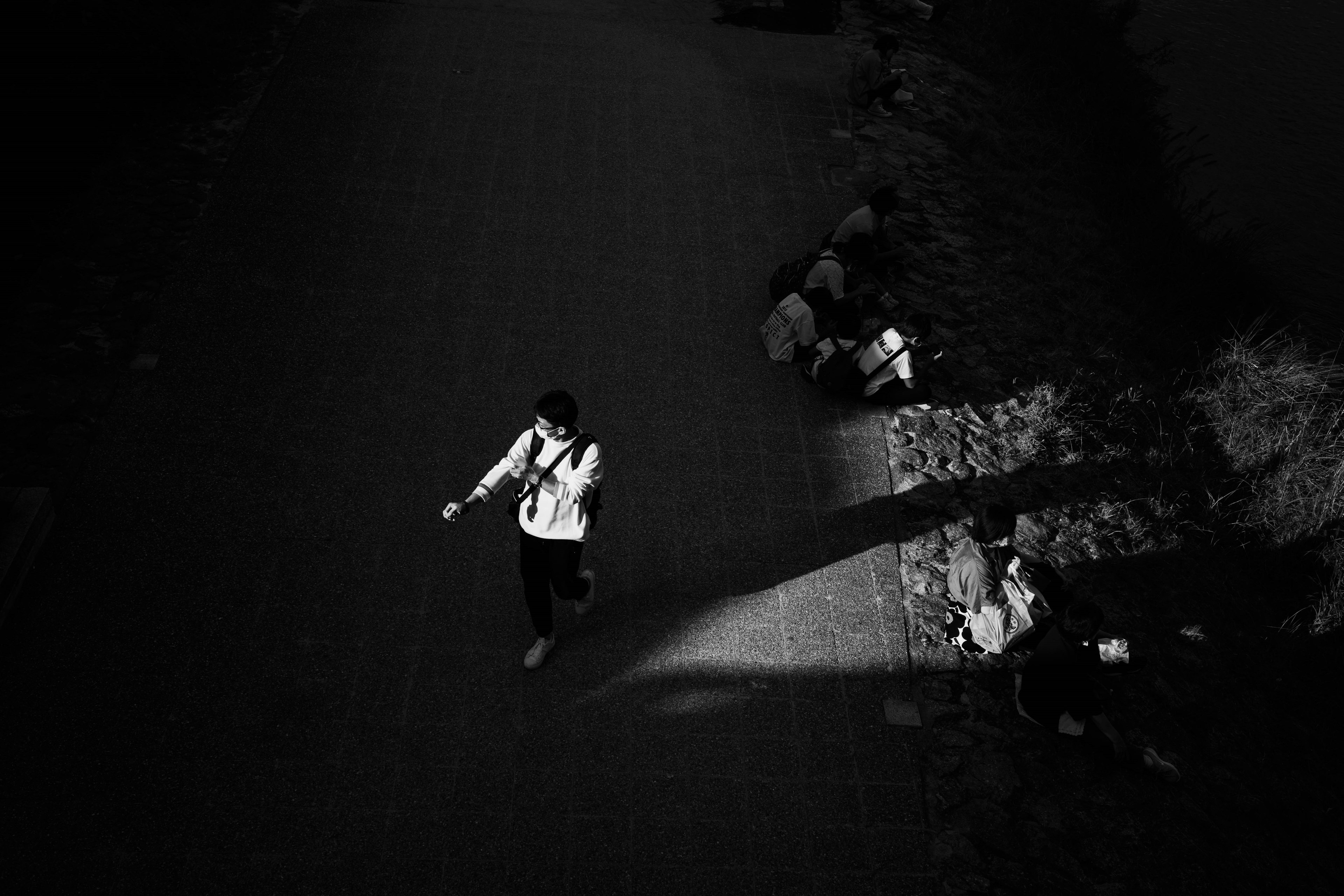 Black and white photo of a person walking on a path with shadows