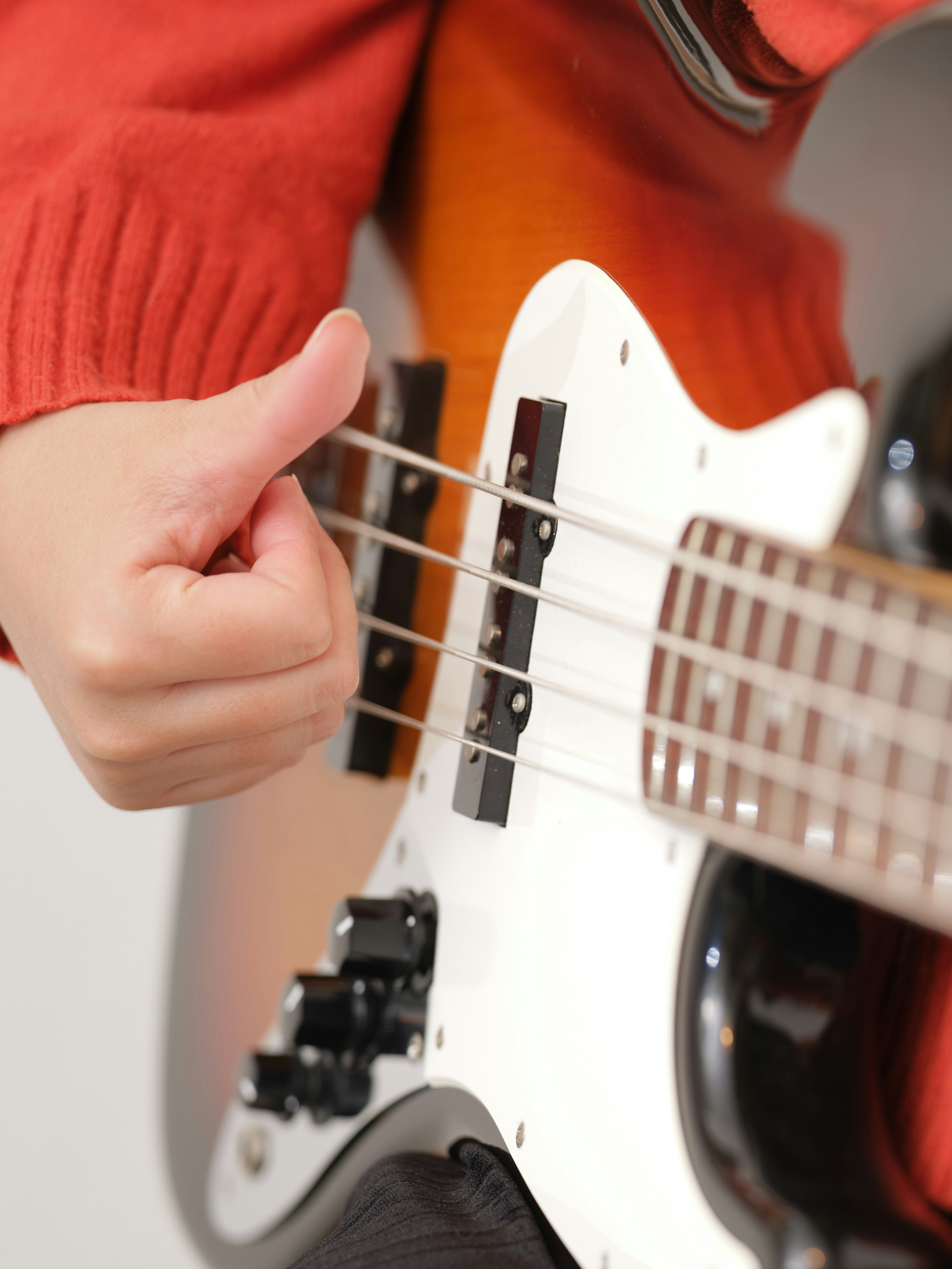 Hand, die eine Bassgitarre mit einem orangefarbenen Pullover spielt