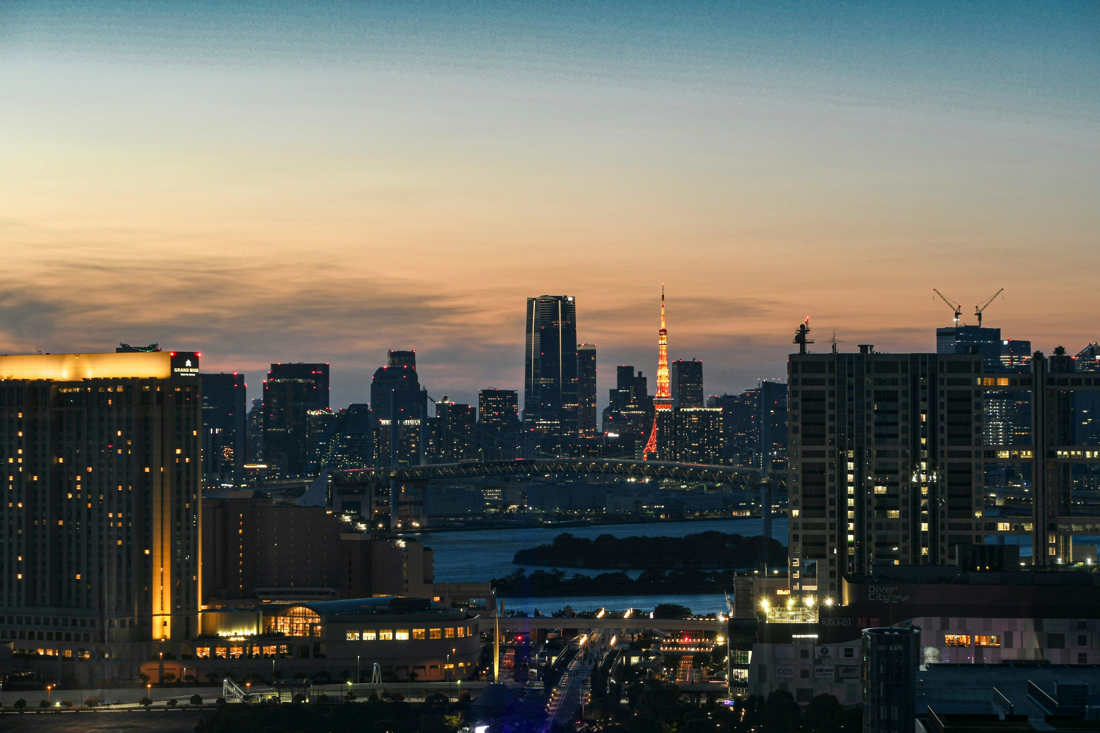 Garis langit Tokyo saat matahari terbenam dengan gedung-gedung yang diterangi dan Menara Tokyo