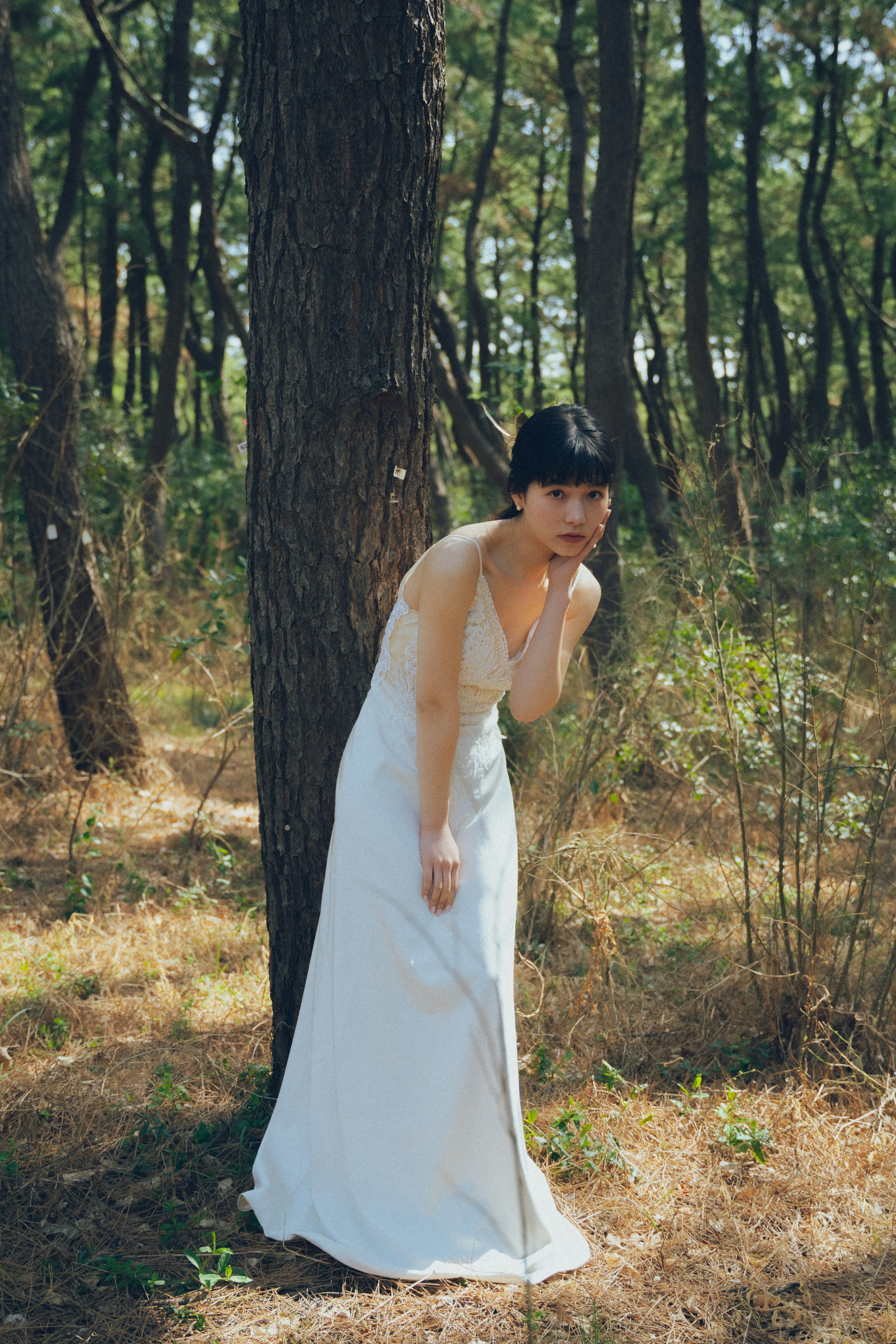 Una mujer con un vestido blanco de pie junto a un árbol en un entorno natural