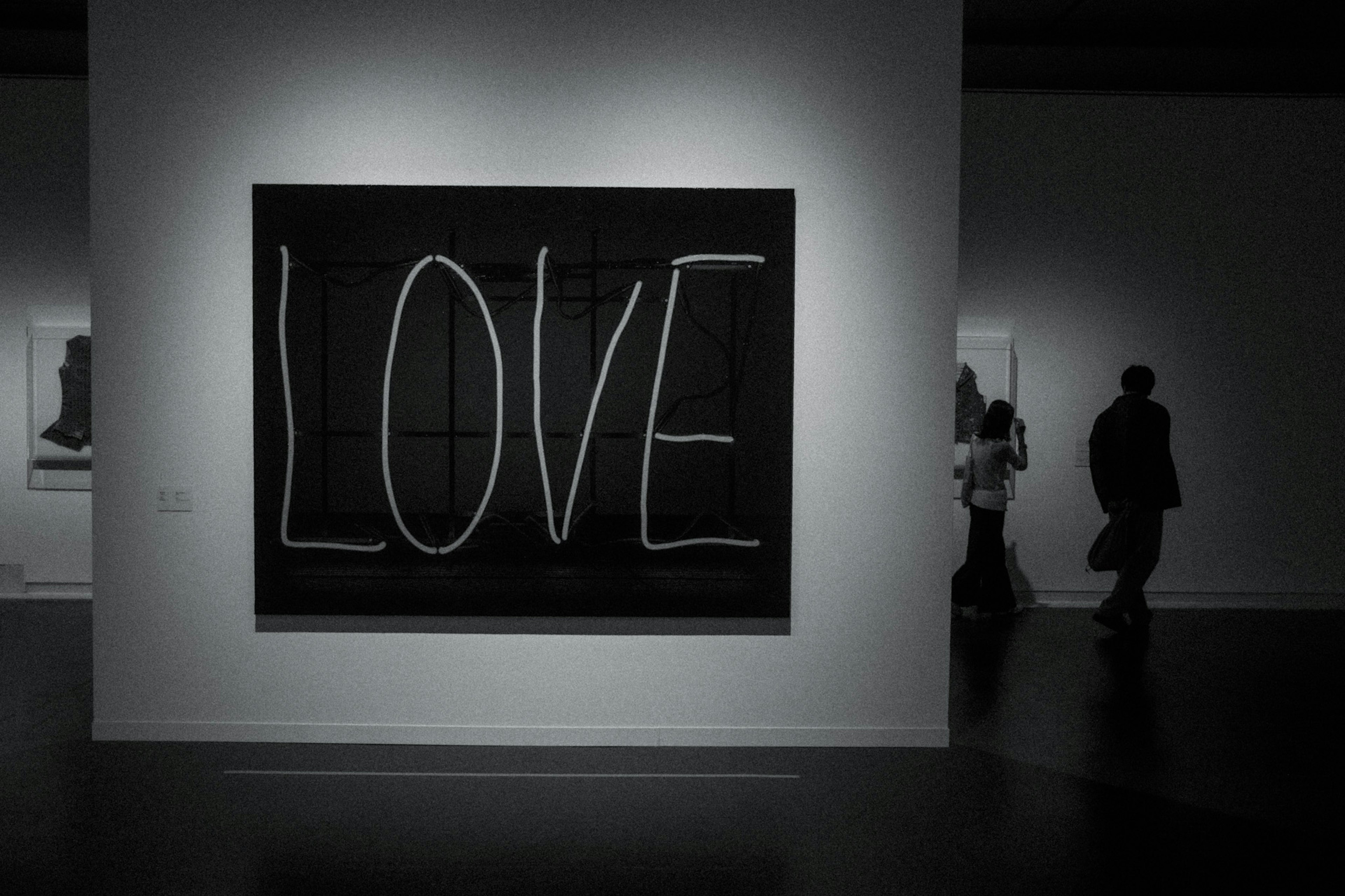 Obra de arte en una galería con la palabra LOVE en grandes letras blancas sobre fondo negro y visitantes