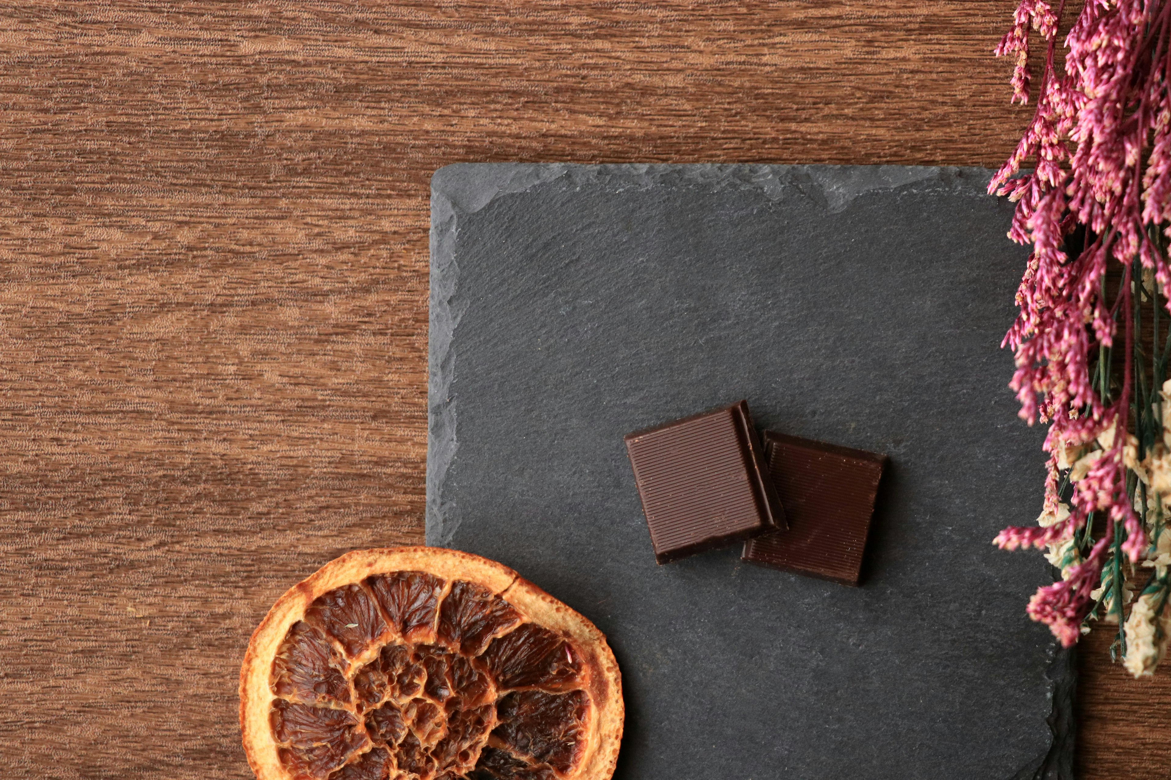 Pépites de chocolat noir sur une assiette en ardoise avec orange séchée et fleurs