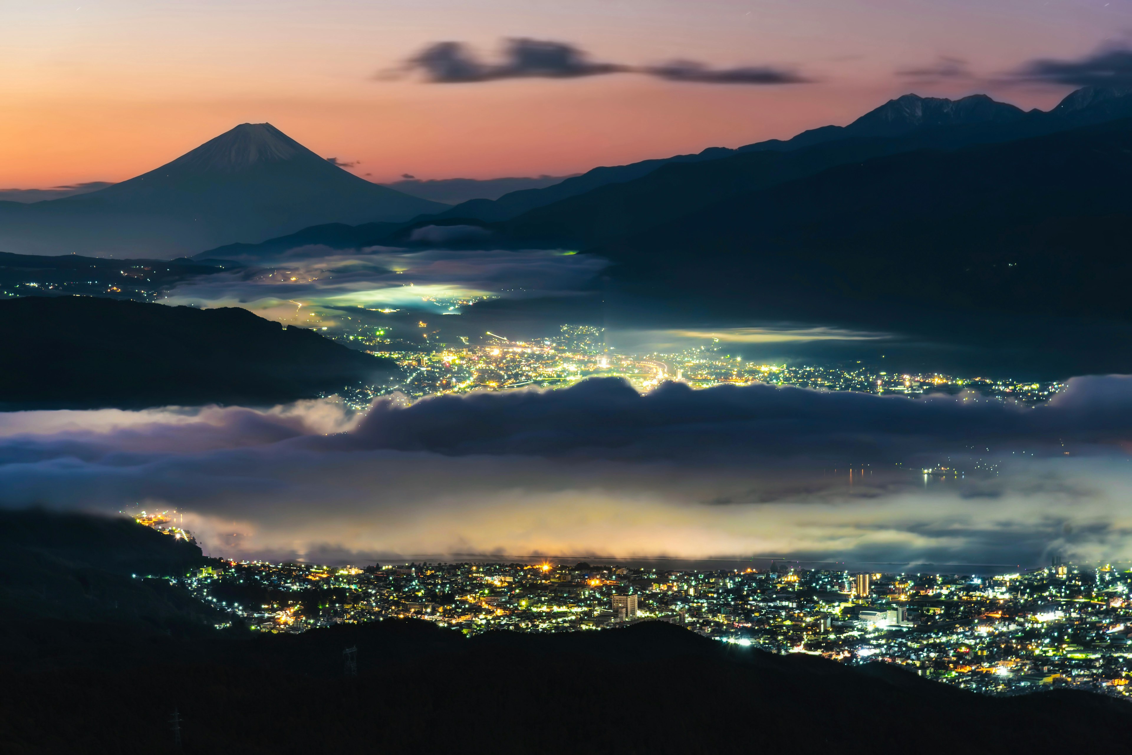 夕暮れ時の山々と雲海に囲まれた都市の夜景