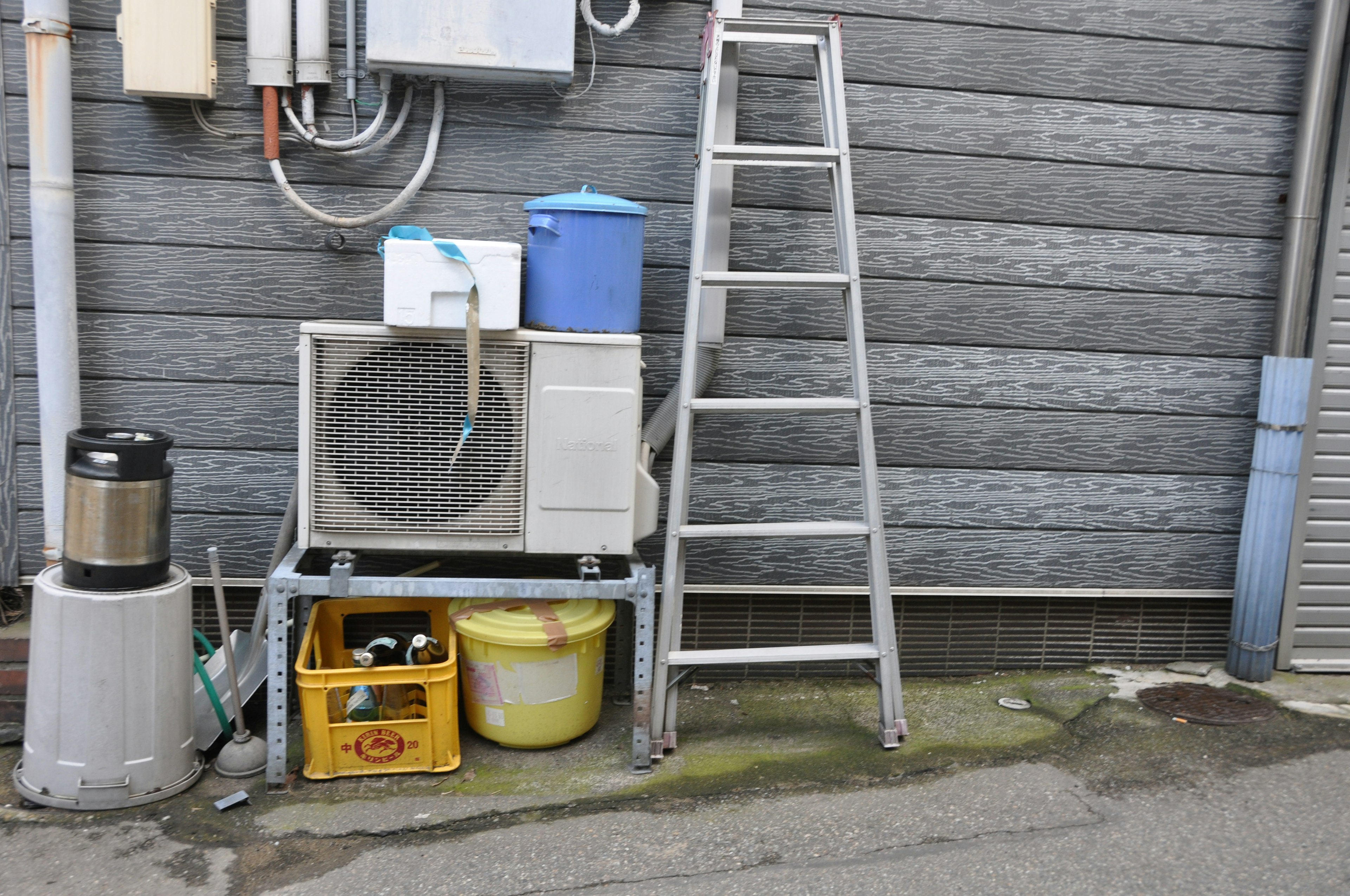 Metal ladder and various containers beside an outdoor wall