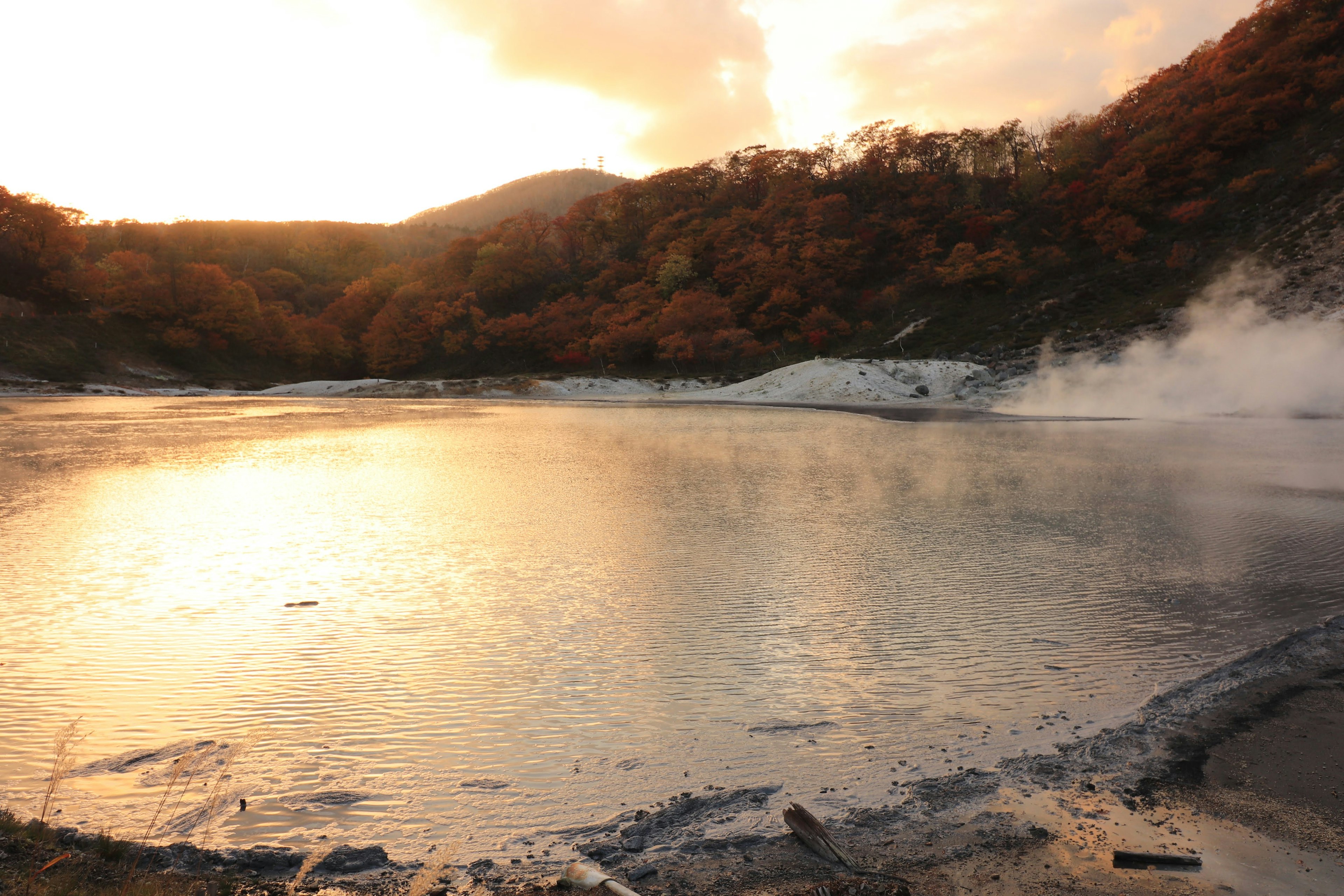 Hot spring lake reflecting sunset with surrounding autumn foliage