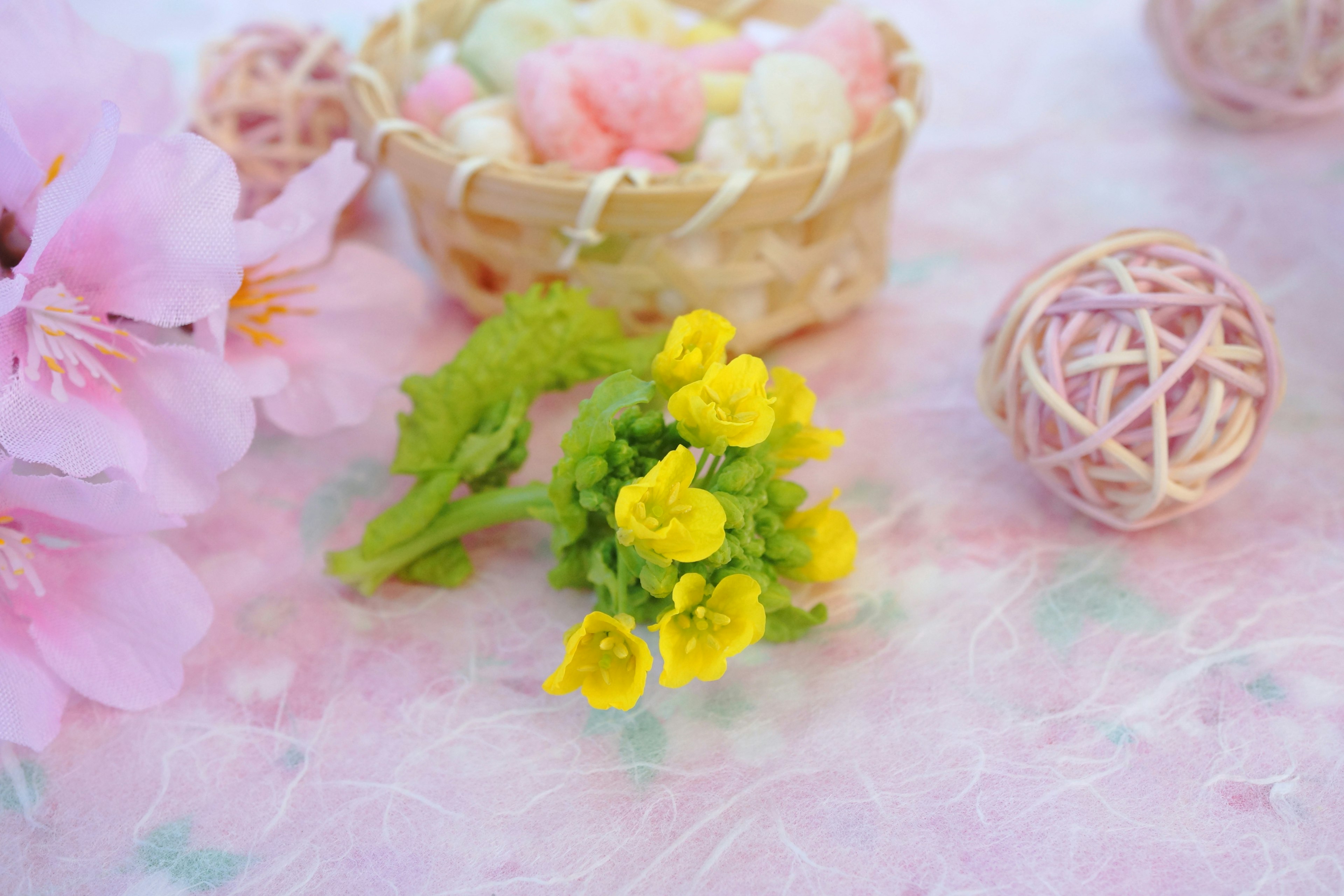 Ein kleiner Strauß gelber Blumen umgeben von rosa Blütenblättern einem geflochtenen Korb und dekorativen Bällen