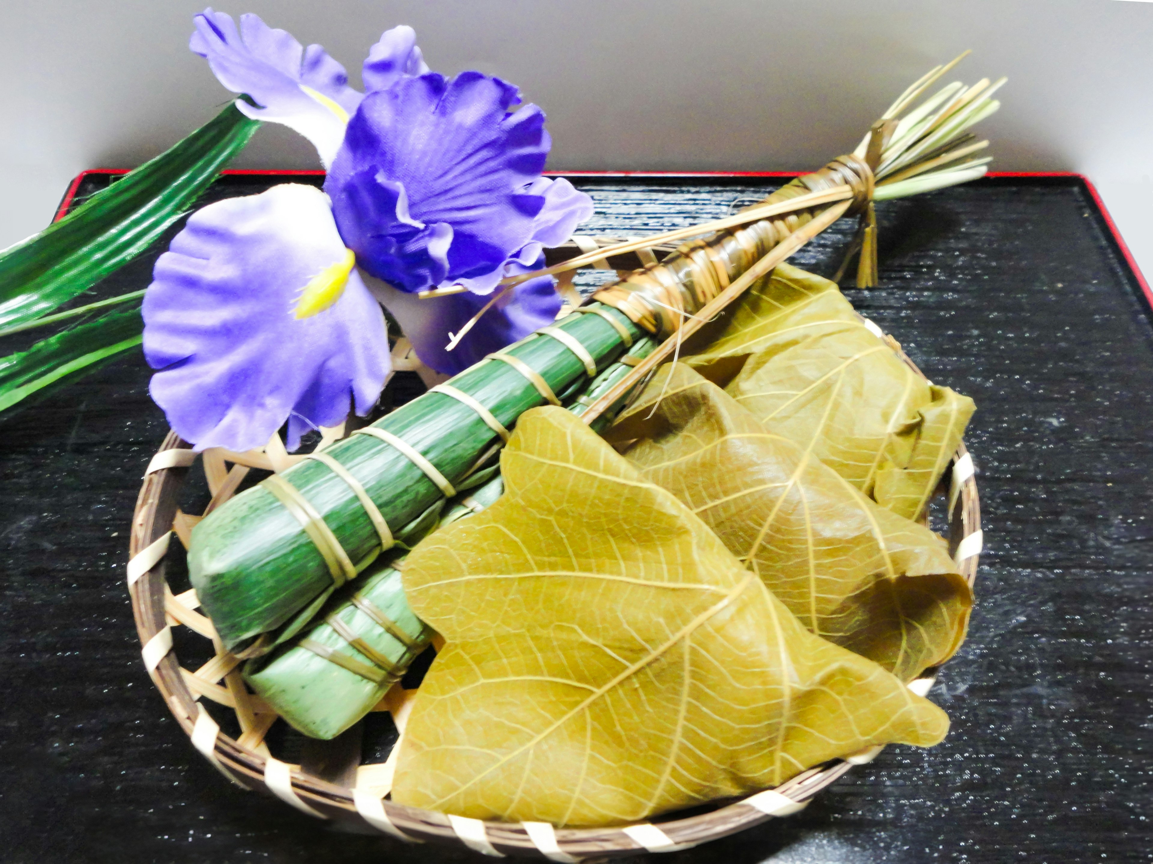 A basket containing purple flowers and green leaf wraps