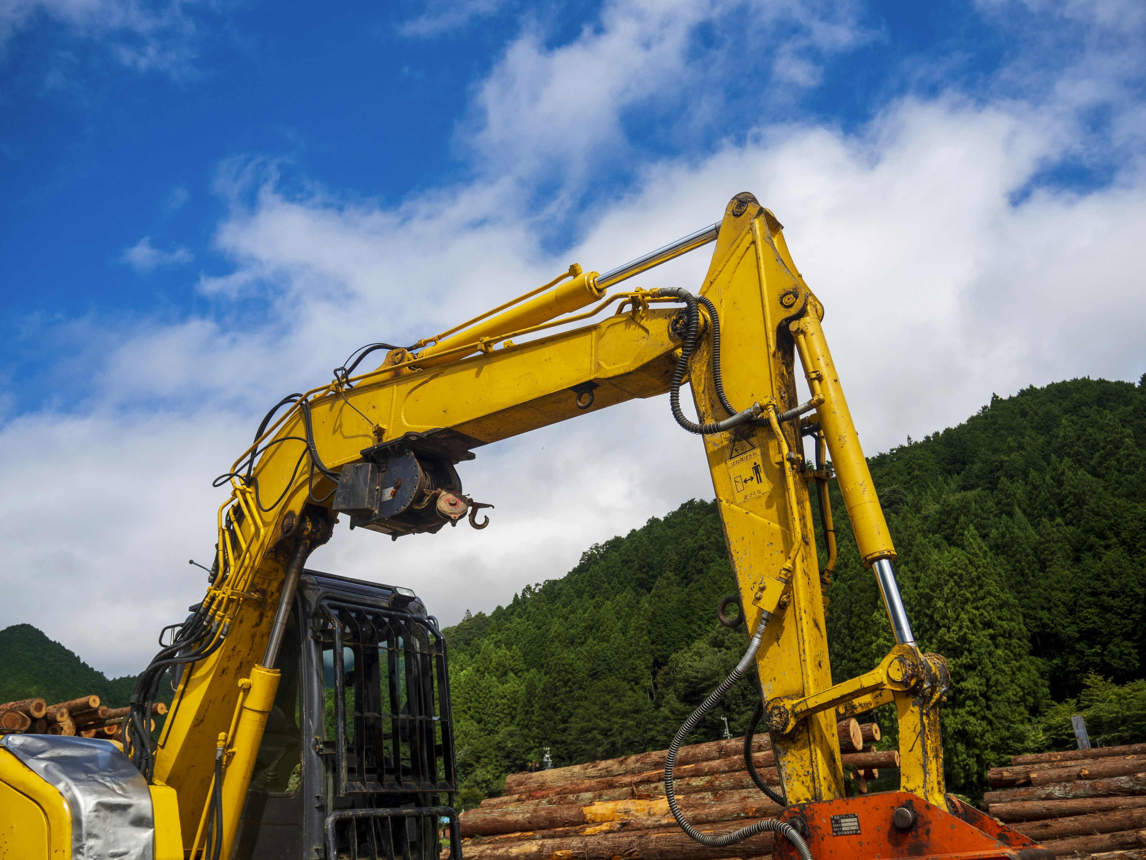 Lengan crane kuning mengangkat kayu di bawah langit biru