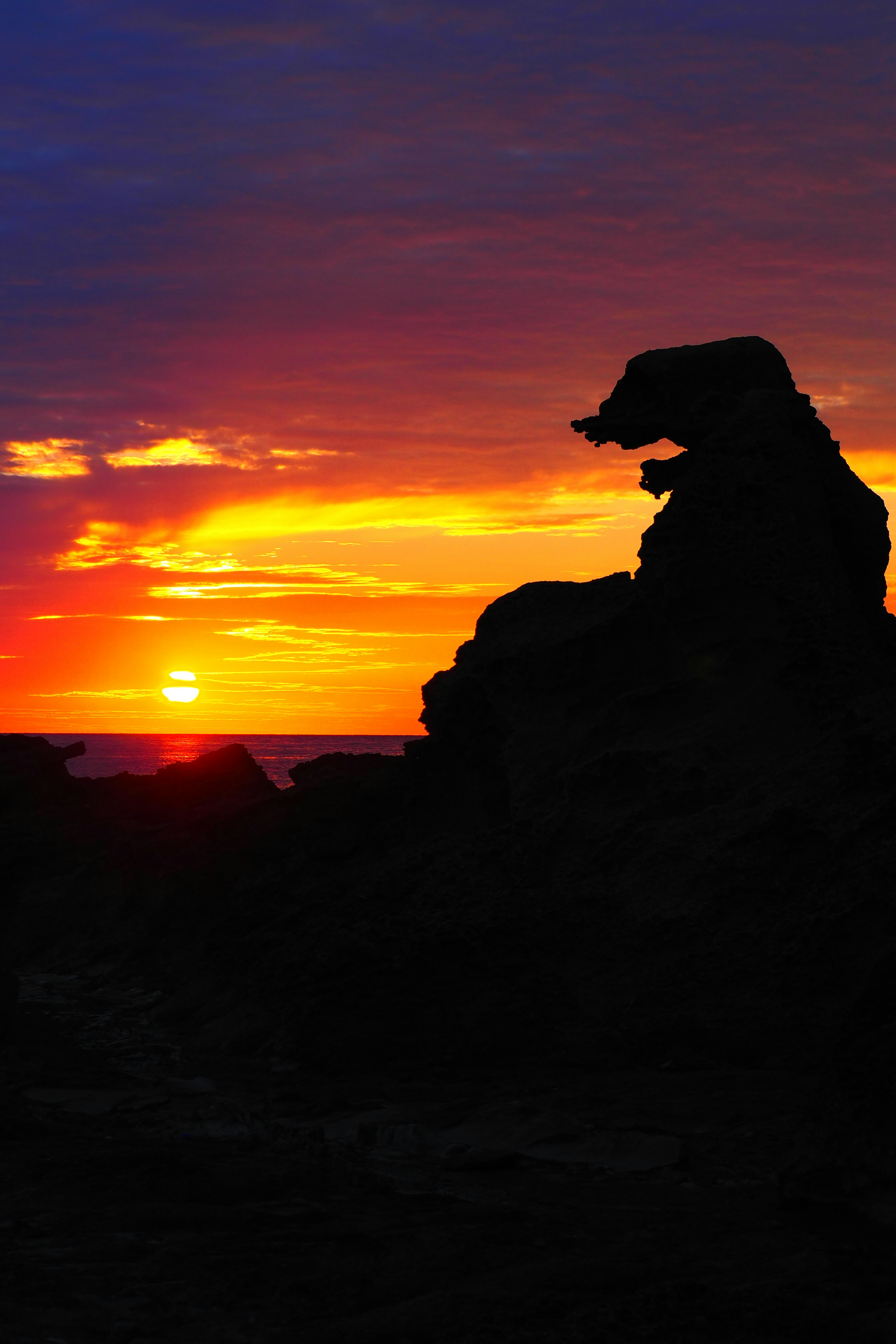 Silhouette of rock formation against a vibrant sunset