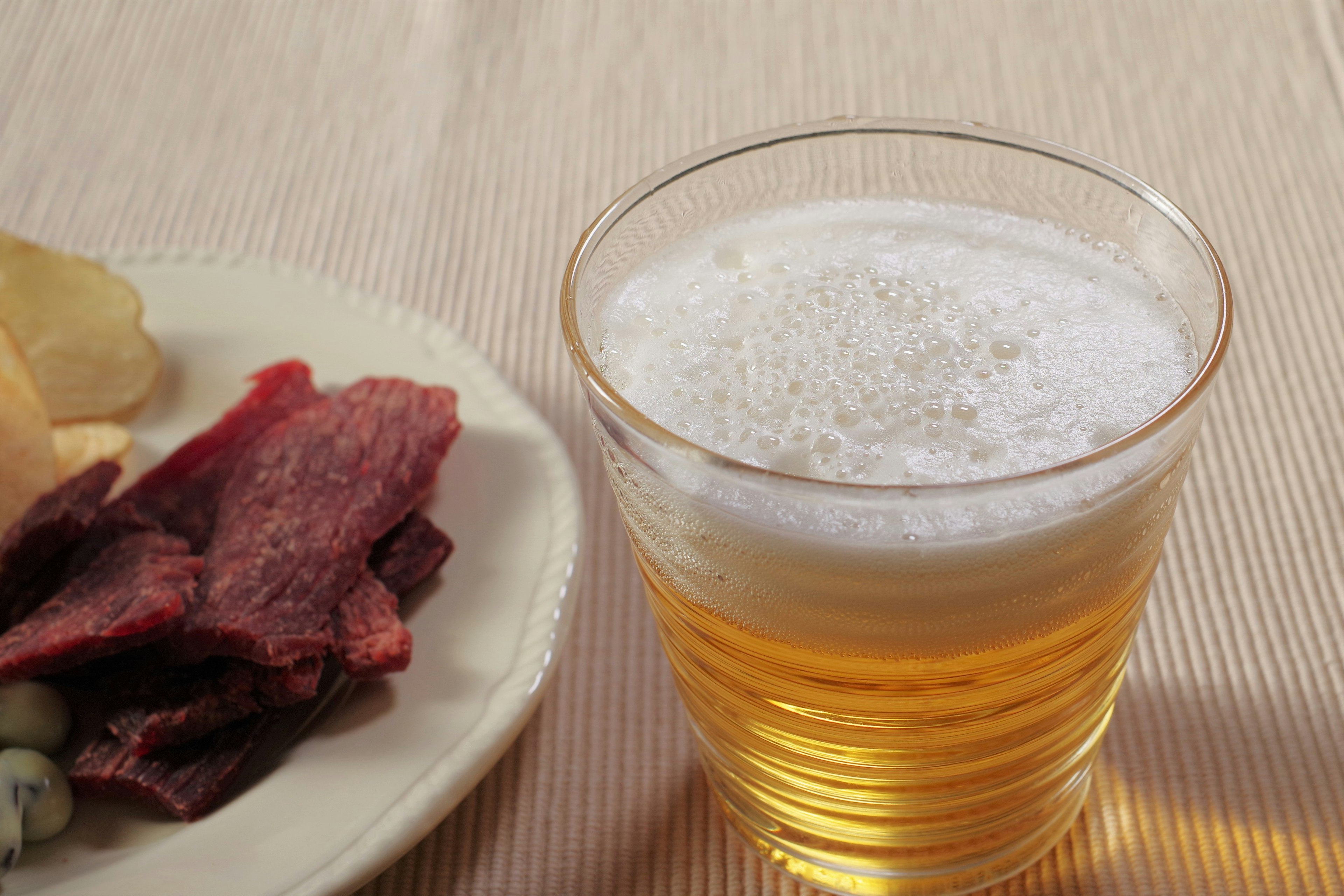 A glass of beer next to a plate of snacks including chips and dried meat