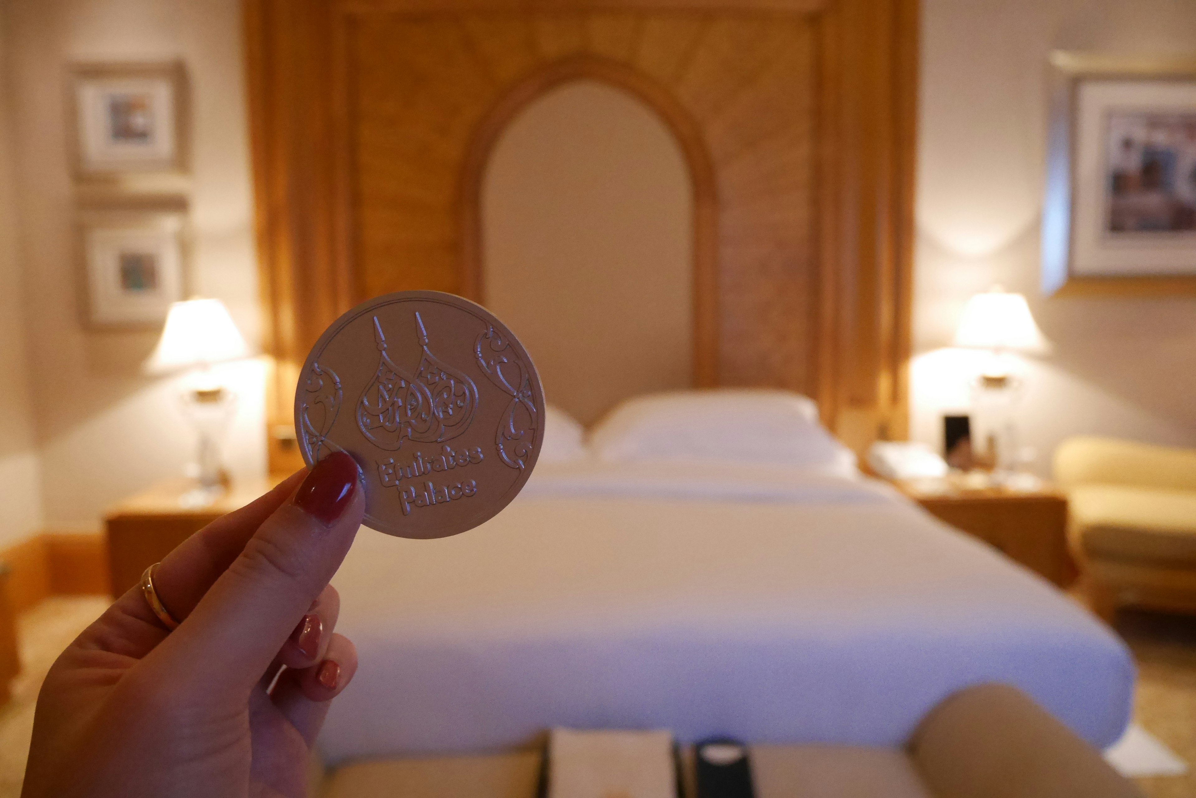 A hand holding a coin in front of a luxurious bedroom