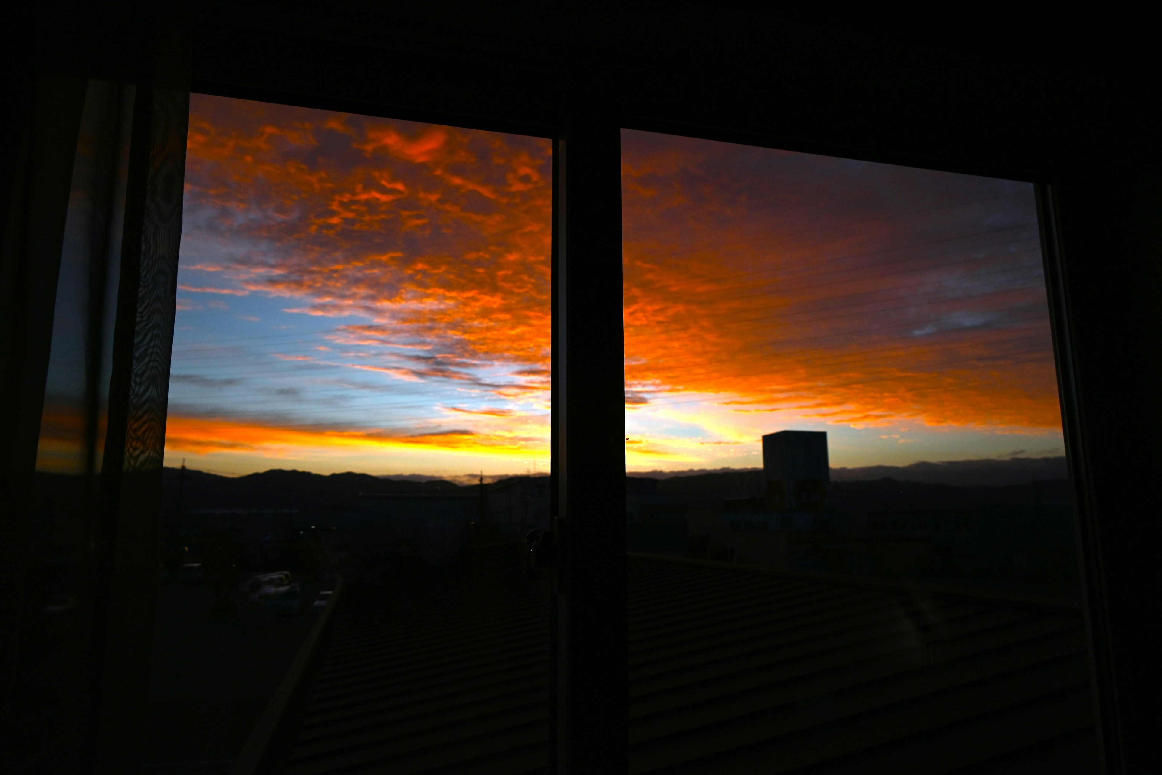 Vista del atardecer a través de una ventana tonos vibrantes de naranja y azul siluetas de montañas