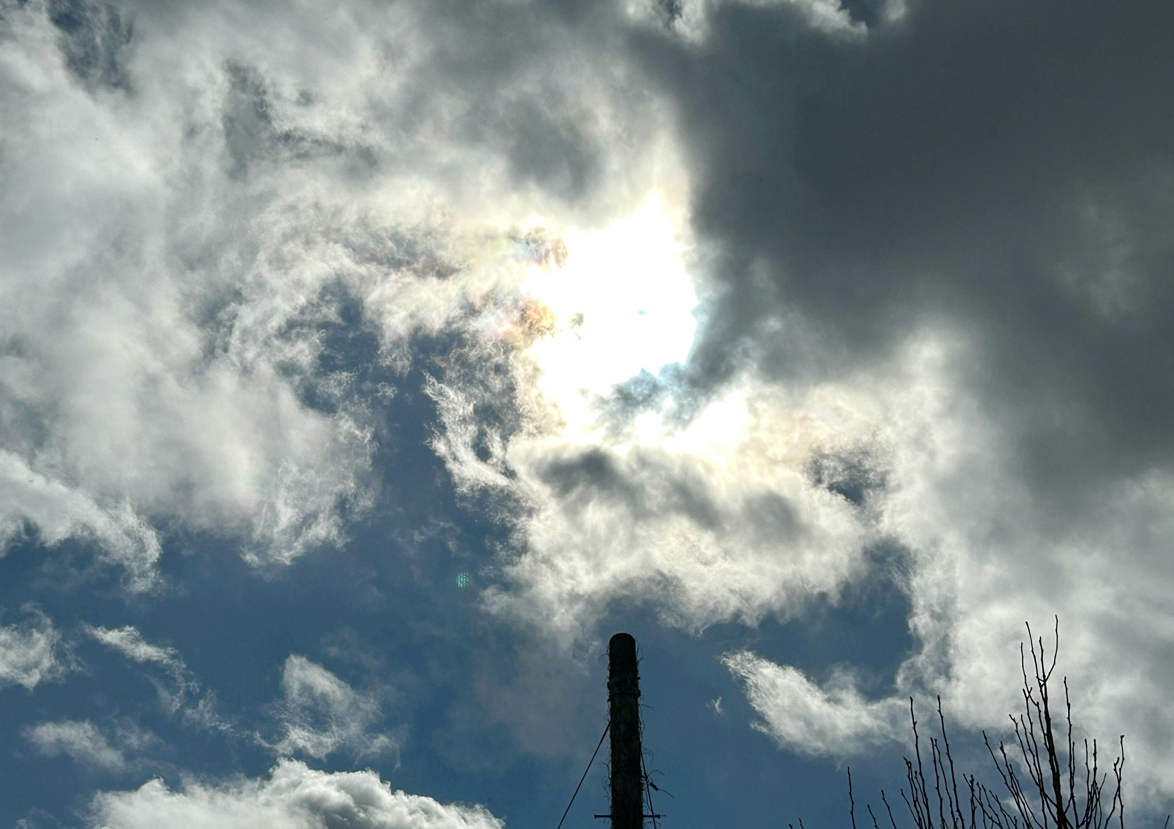 Ein blauer Himmel mit Wolken um die Sonne und einem Schornstein