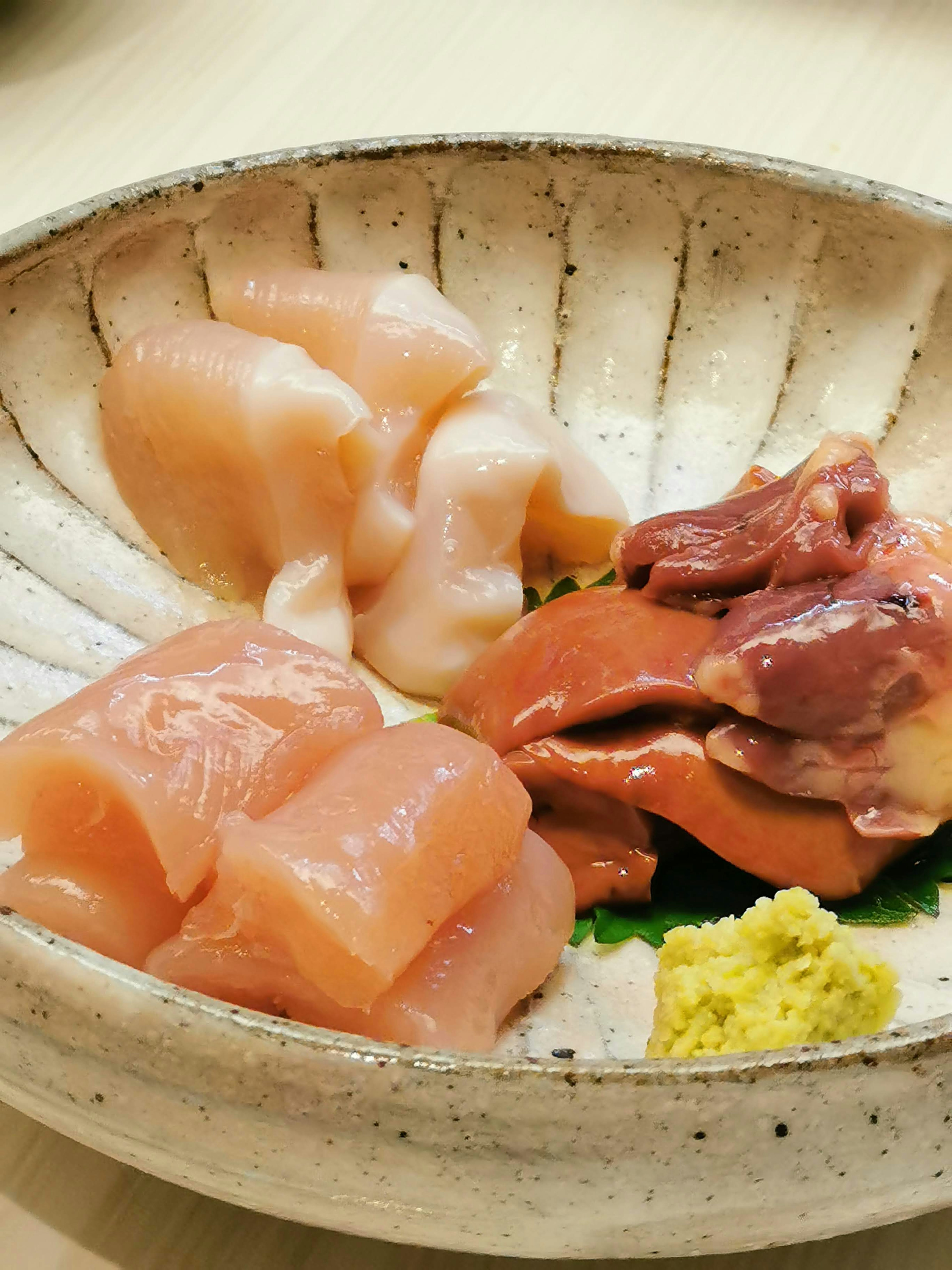 Fresh chicken sashimi presented on a white dish with wasabi